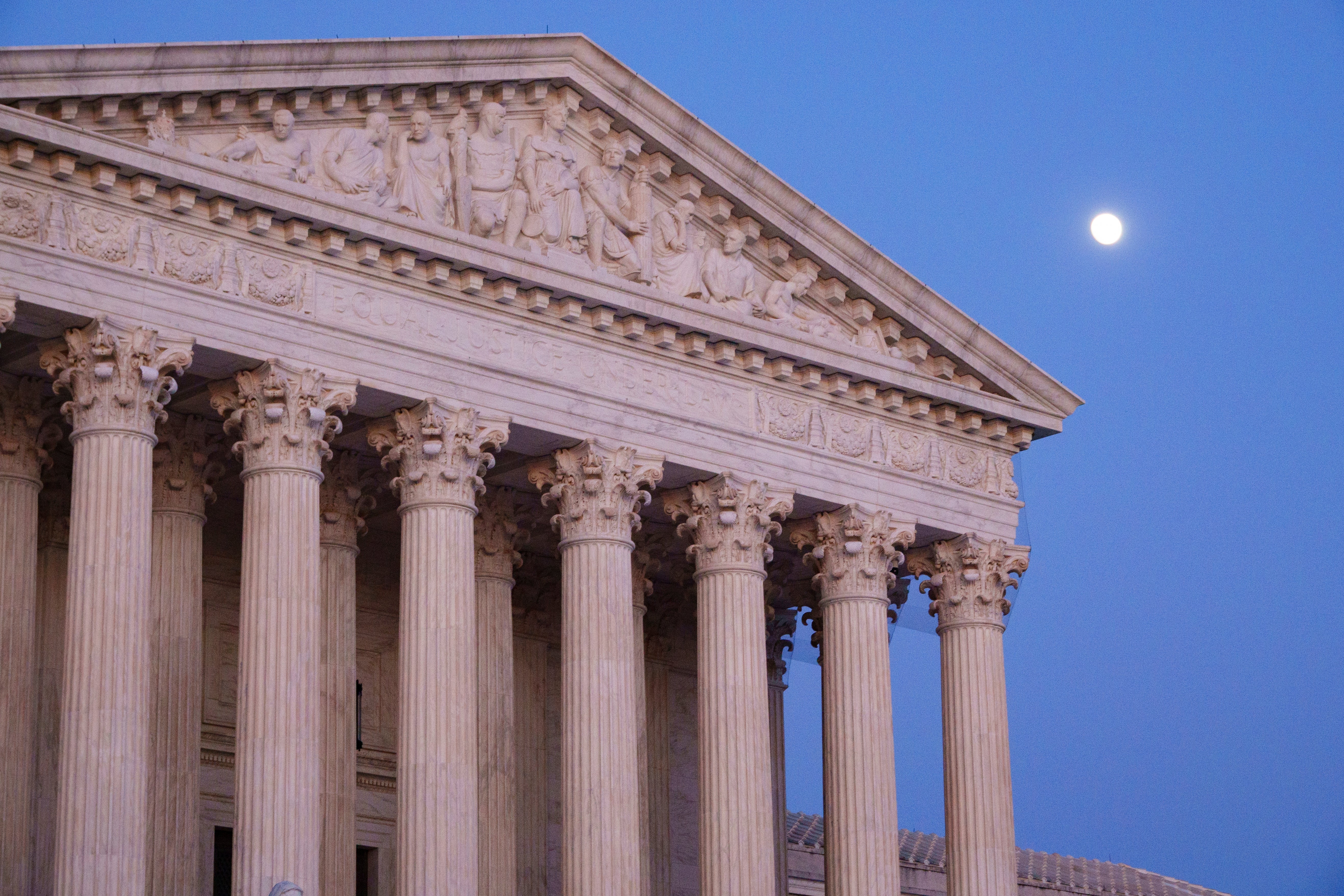 U.S. Supreme Court gathering nether a wide entity astatine dusk, satellite visible. Classic architectural columns and triangular pediment with sculptures