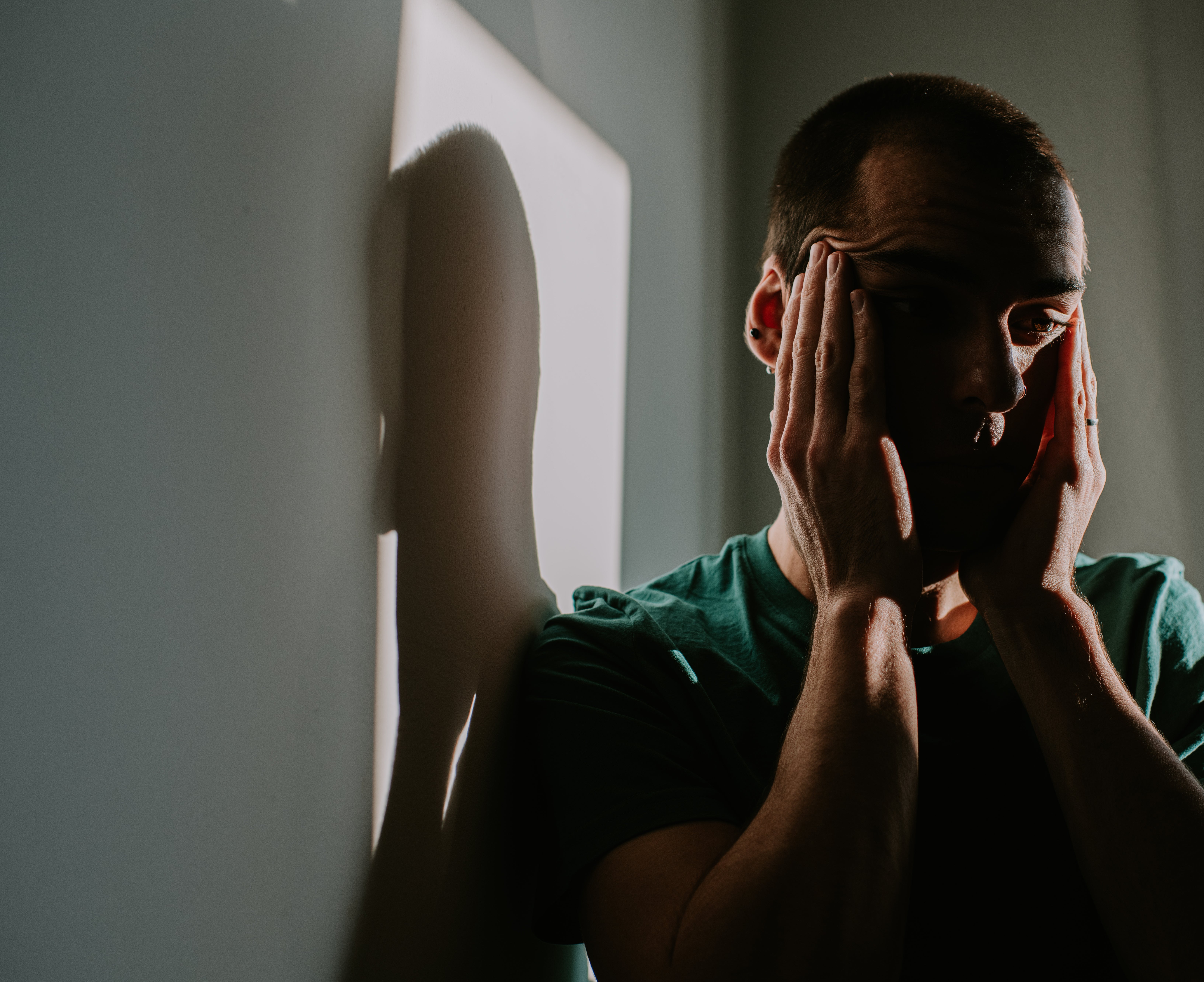 Person lasting against a partition with hands connected face, casting a shadow. The temper appears contemplative oregon distressed