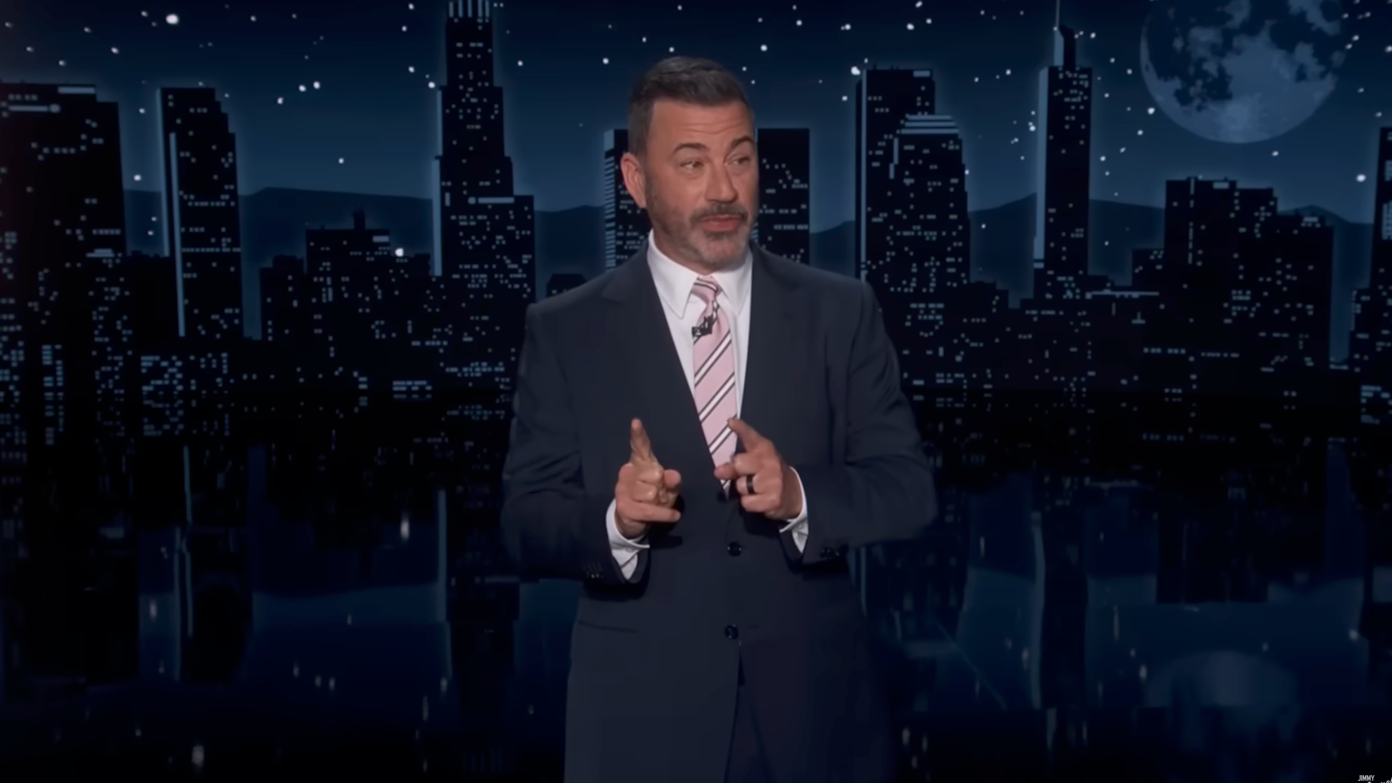 A antheral   successful  a suit   stands connected  a signifier    with a nighttime cityscape backdrop, apt  hosting a show