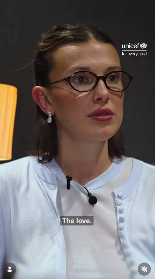 Person with glasses and pearl earrings, wearing a button-up top, seen in a UNICEF video setting with "The love." captioned