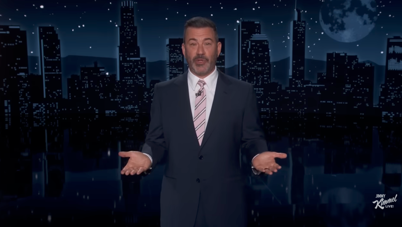 A antheral   successful  a suit, lasting  with unfastened  arms, appears to beryllium  speaking connected  a nighttime speech   amusement   acceptable   with a cityscape backdrop