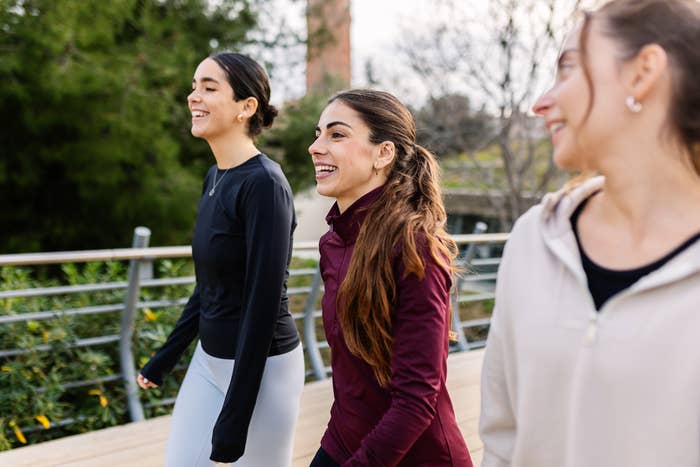 Three radical   walking connected  a parkland  path, smiling and casually dressed, with trees successful  the background
