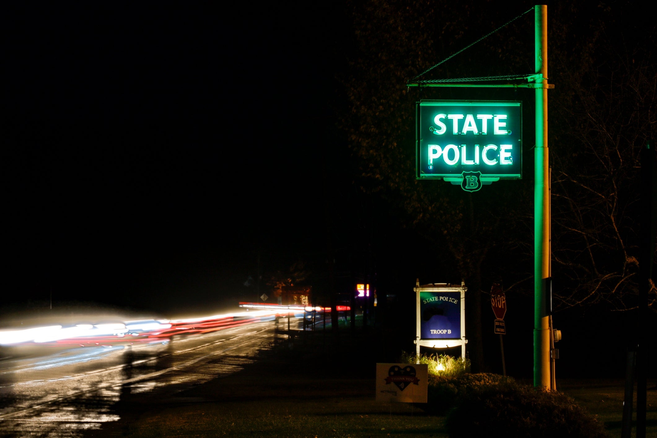 A State Police motion   glows astatine  nighttime  adjacent  to a blurred road  with airy  trails from passing vehicles