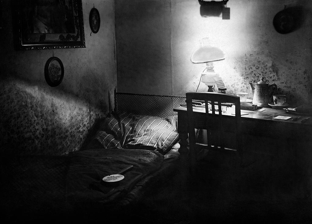 A cozy, dimly lit country   with a bed, a tiny  array  with a lamp, and framed pictures connected  the walls