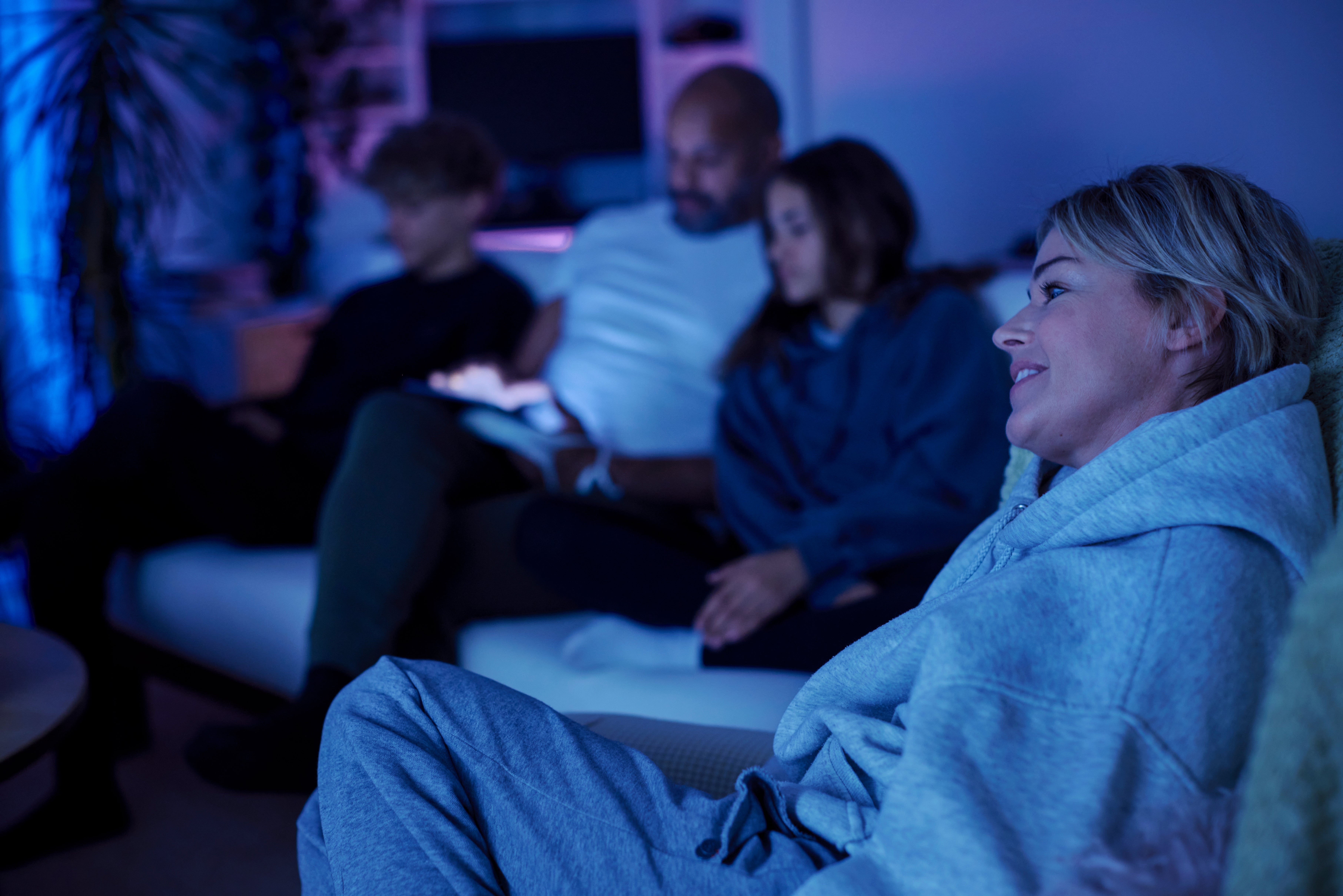 A household  of 4  relaxes connected  a sofa  successful  a dimly lit surviving  room, with 1  subordinate   looking contented  portion    others absorption   connected  a tablet