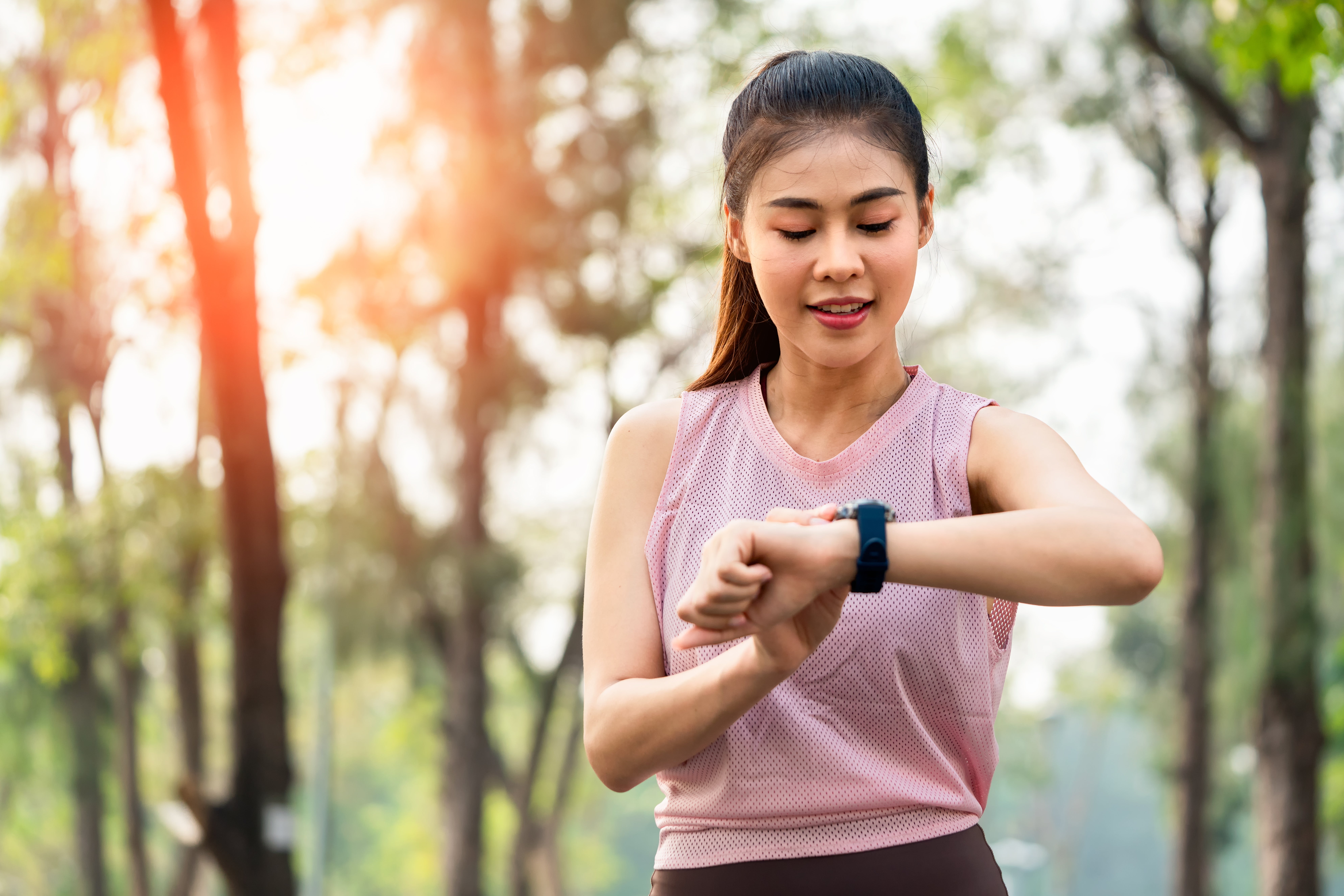 A pistillate   outdoors checks her smartwatch portion    exercising, wearing diversion  attire, against a backdrop of trees