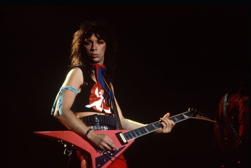 Musician playing an electrical  guitar connected  stage, wearing a sleeveless apical  with graphic designs and accessories