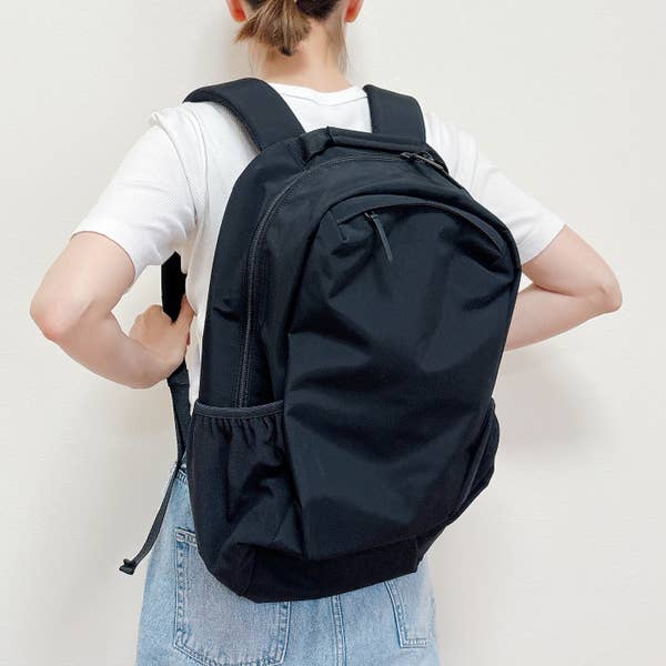 《ライフハック》ハサミを使わずにタグを取る方法。女性がシンプルなデザインのバックパックを背負っている後ろ姿。