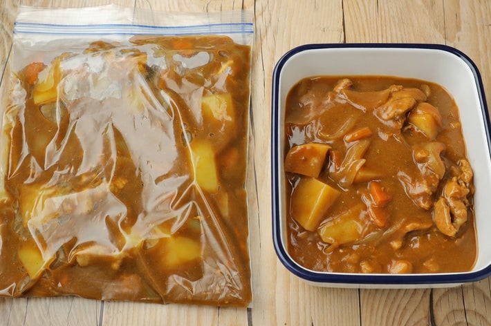保存袋に入ったカレーと食器に盛られたカレーが、木製のテーブル上に並べられている。