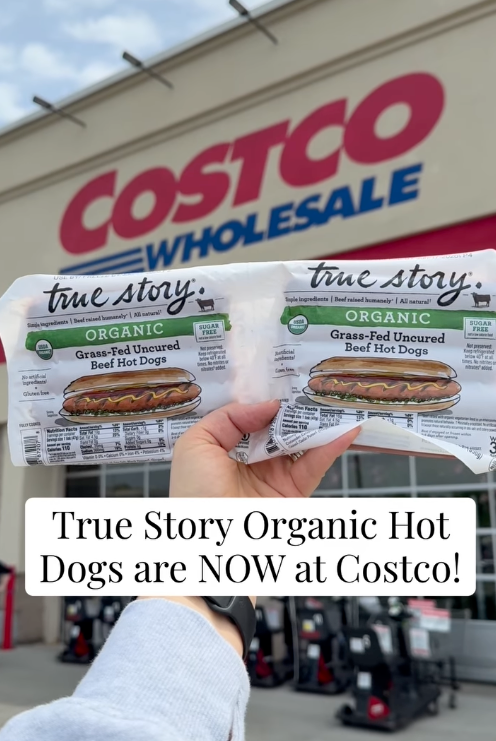 Packages of True Story Organic Hot Dogs held in front of a Costco store, highlighting their availability at Costco