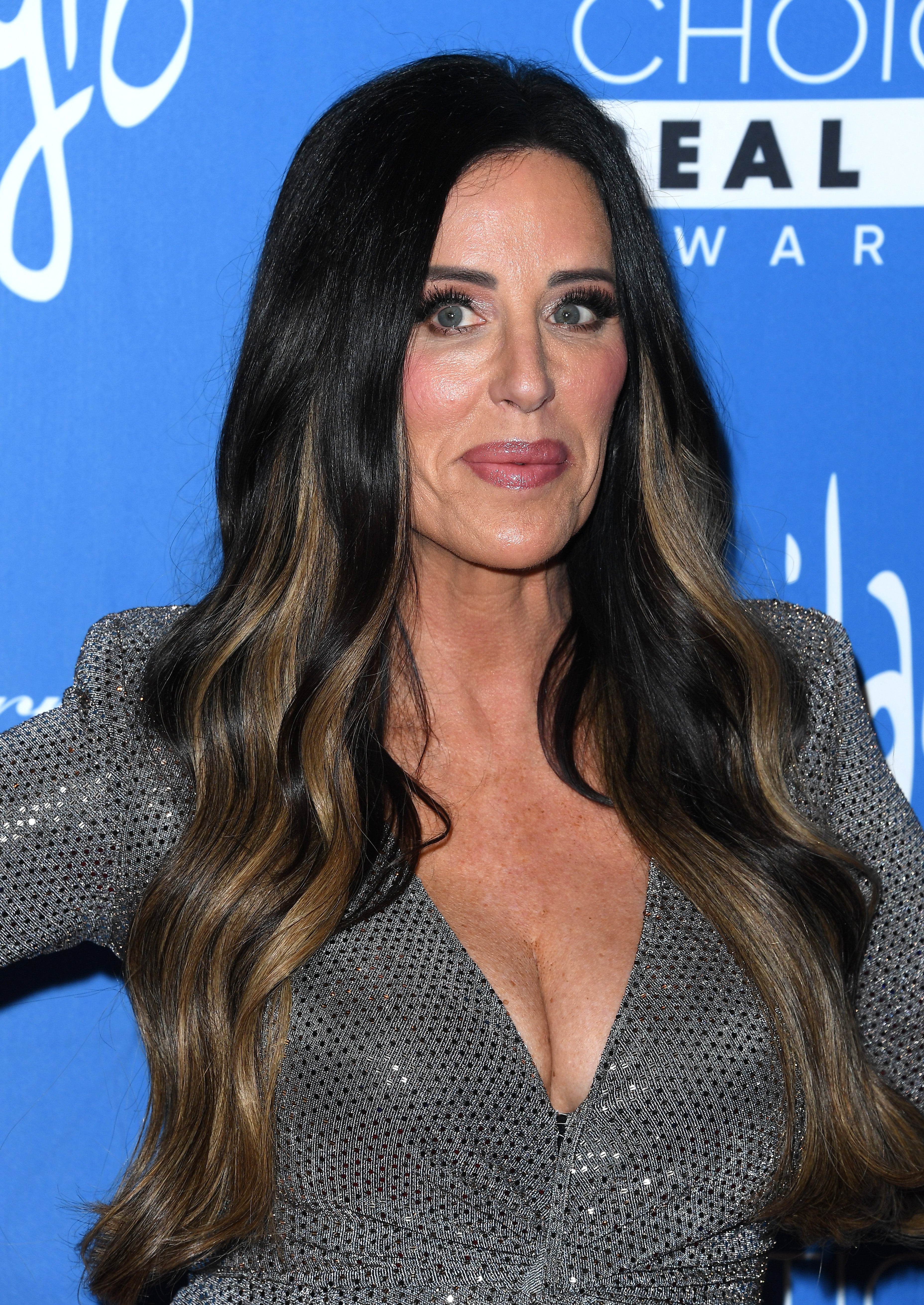 Person successful a glittering V-neck formal with long, styled hairsbreadth poses astatine an lawsuit backdrop