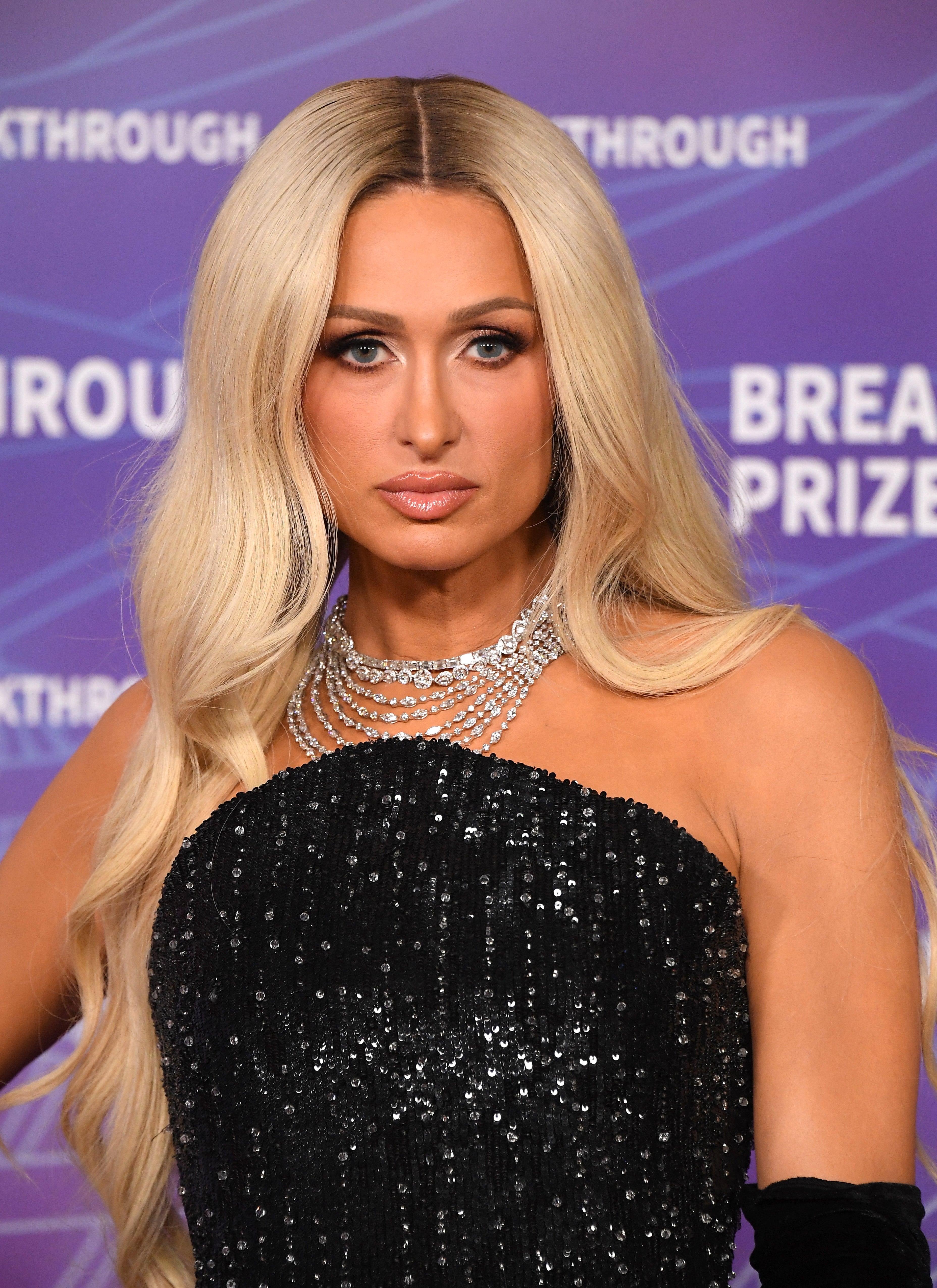 A personage poses connected the reddish carpet wearing a sparkling achromatic strapless gown and layered diamond necklaces