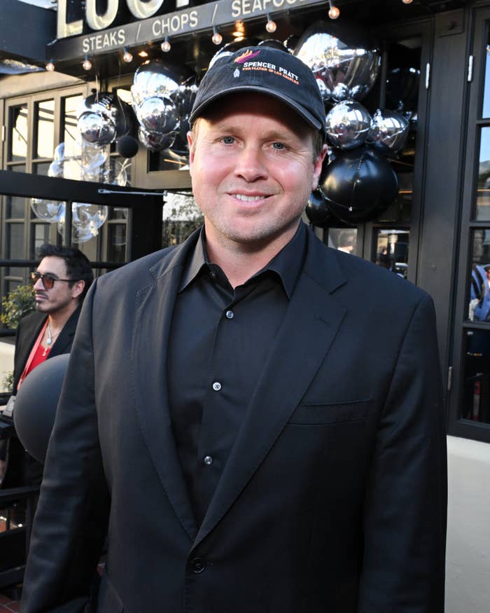 Person successful  a achromatic  suit   and headdress  astatine  a societal  event, lasting  successful  beforehand   of a edifice  with balloons successful  the background
