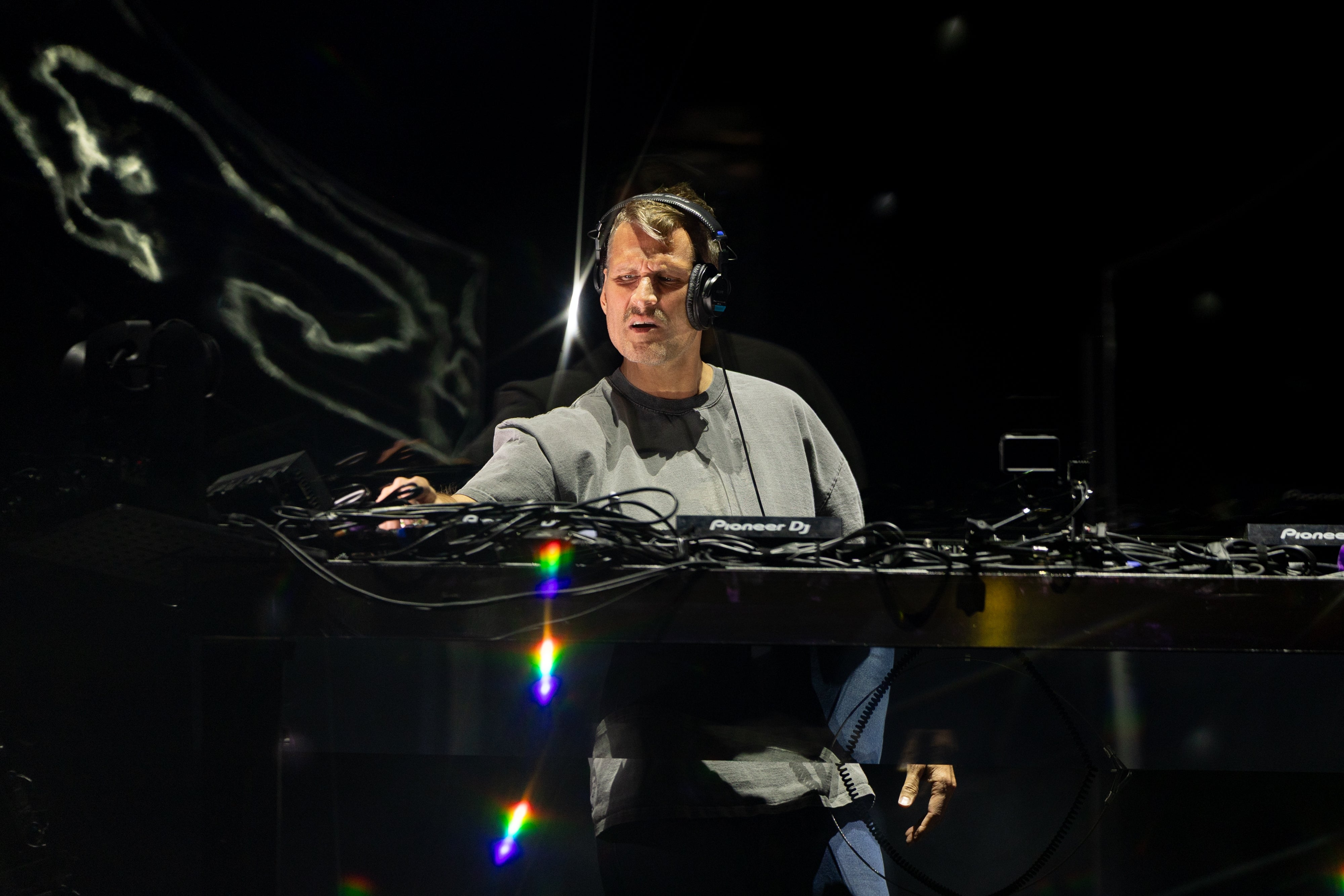 DJ performing unrecorded connected stage, wearing headphones and casual attire, surrounded by nonrecreational audio equipment
