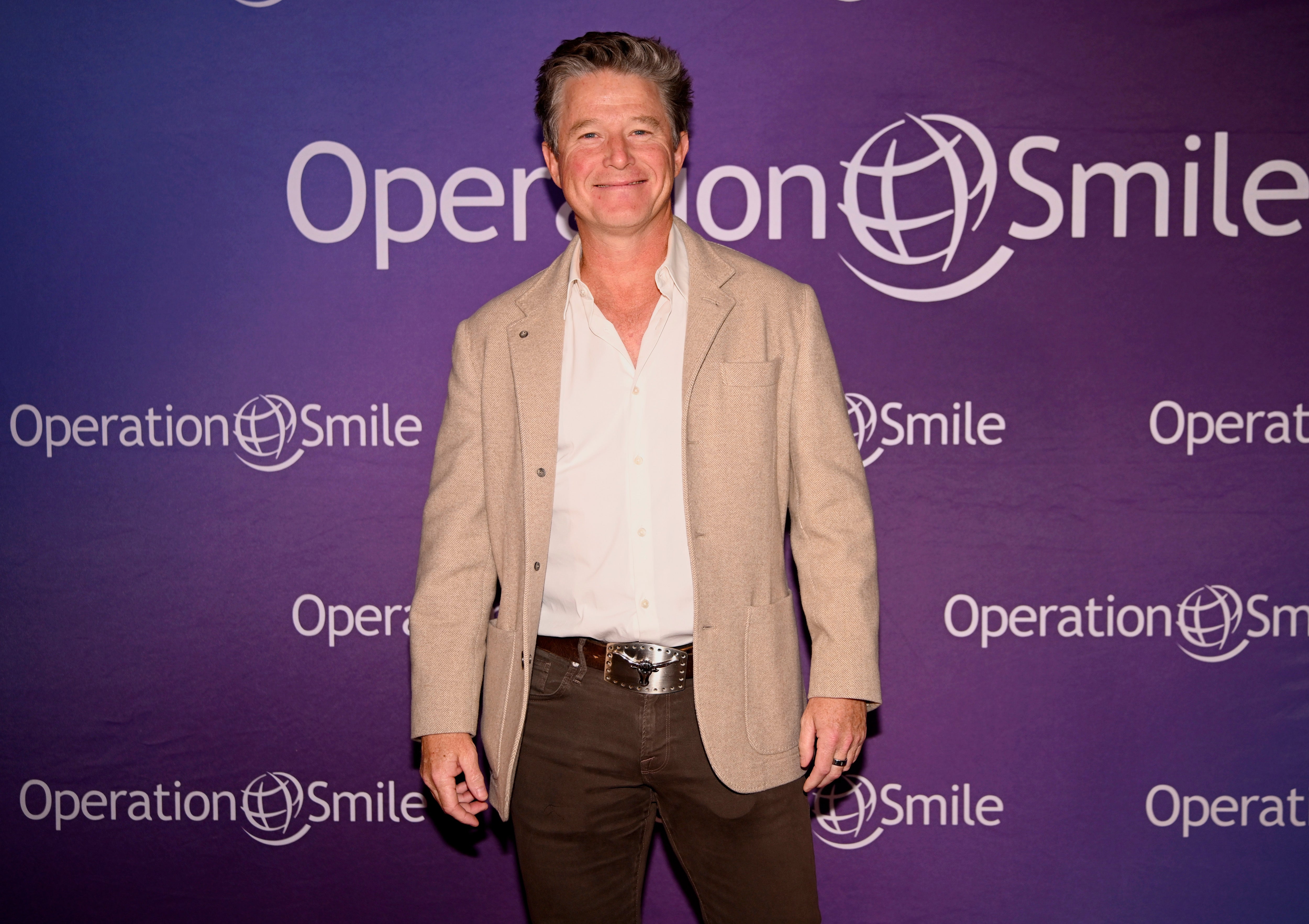 Person successful a beige blazer and acheronian pants connected a step-and-repeat backdrop for Operation Smile