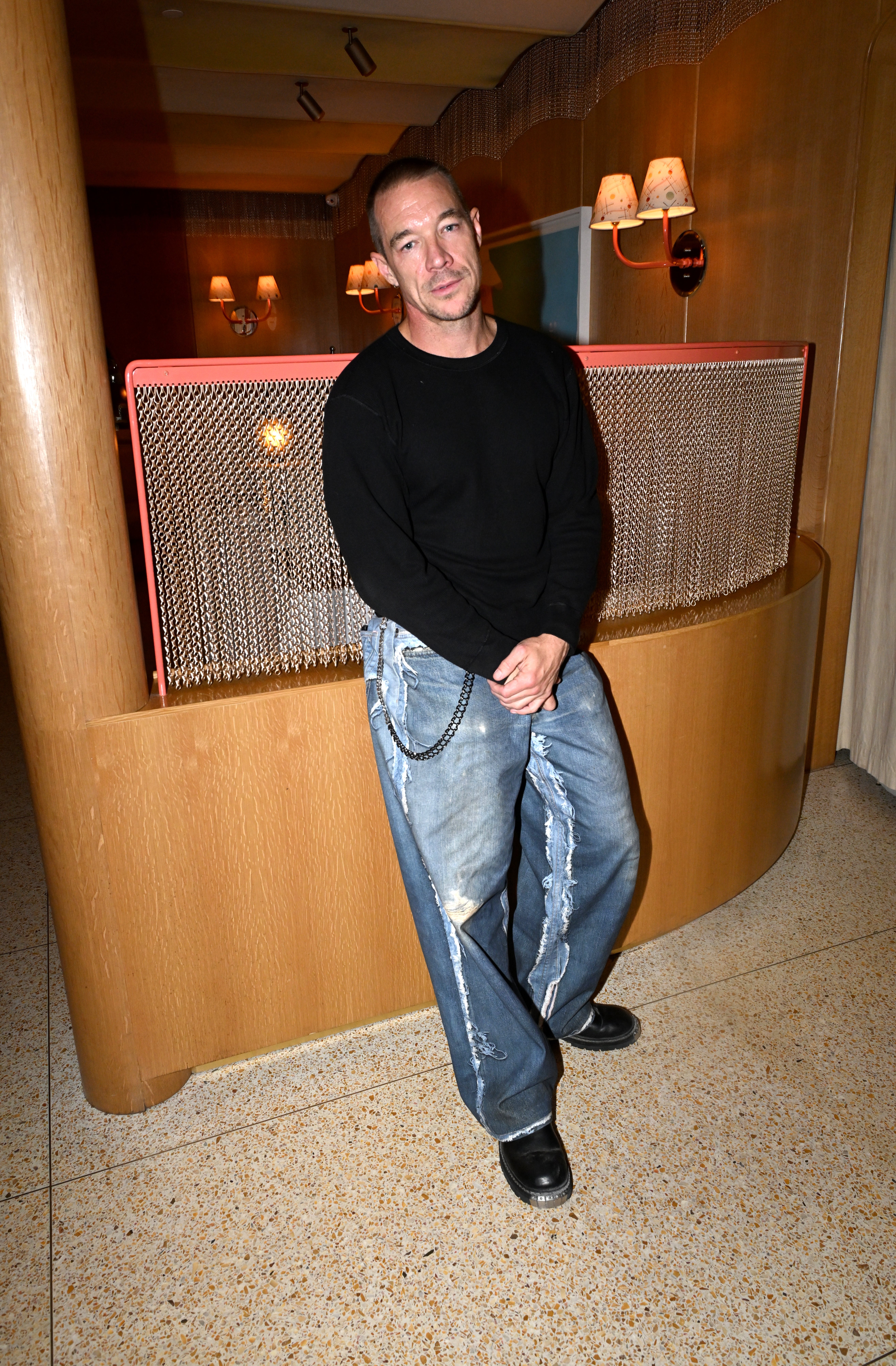 Person successful casual achromatic apical and baggy jeans with concatenation accessory, lasting indoors against a stylish backdrop