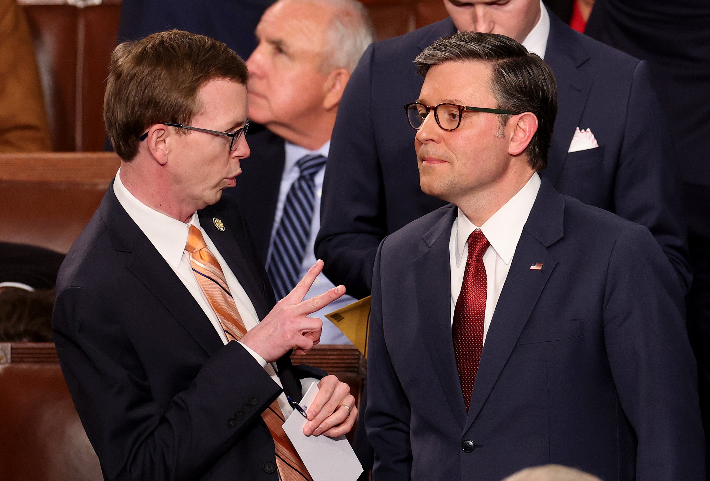 To personer i dress har en samtale i en formell setting, med én gestikulert mens han snakker