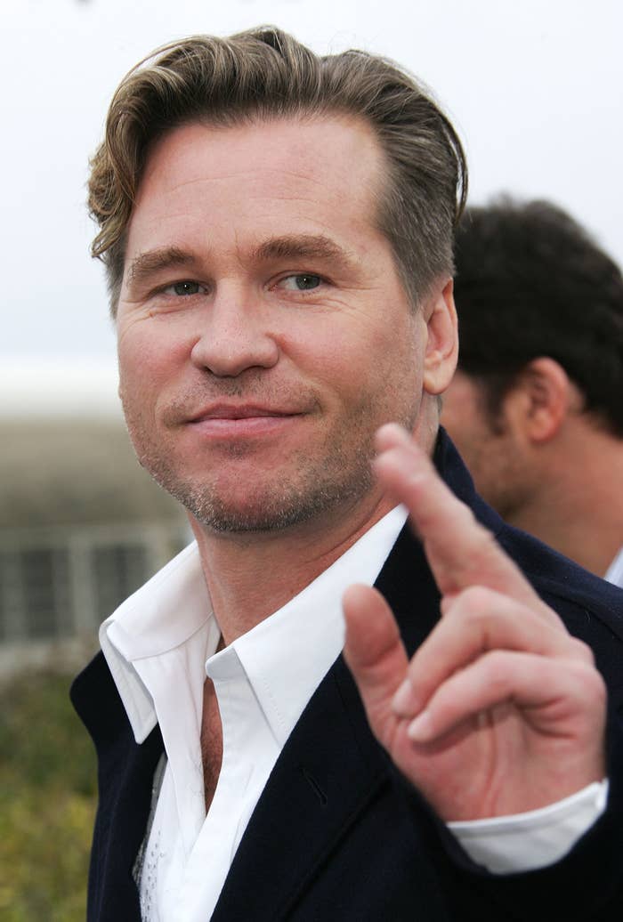 Man in a collared shirt and jacket gestures towards the camera at an event, offering a casual demeanor
