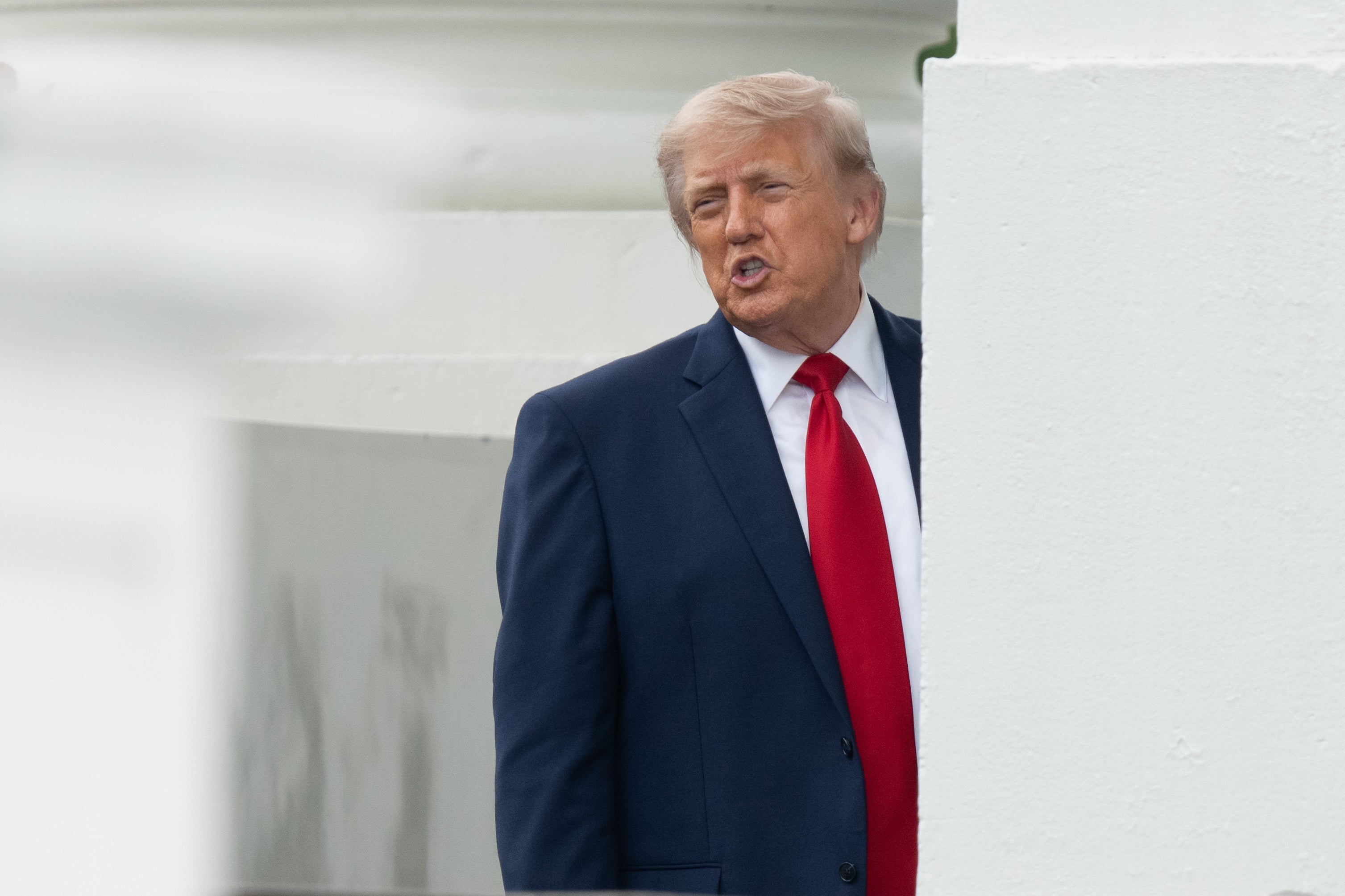 Man successful  a suit   with a reddish  necktie  stands by a building, looking to the side