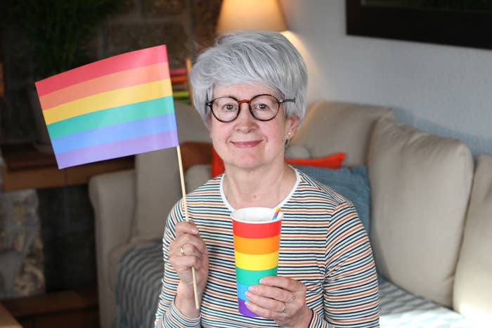 Person with abbreviated  hairsbreadth  holding a rainbow emblem  and cup, sitting connected  a couch. They're wearing a striped shirt, smiling successful  a cozy country   setting