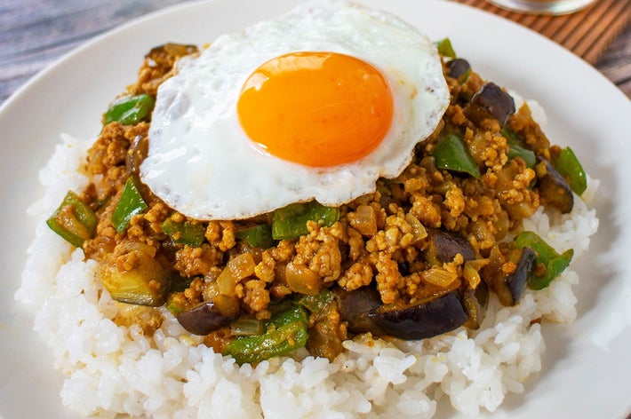 目玉焼きがのったライスプレートに、ひき肉と野菜の炒め物。後ろにアイスティーが見える。