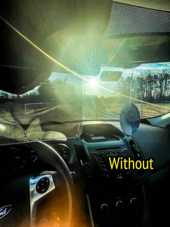 Sunlight shines done  a car   windshield, illuminating the dashboard and steering wheel. Trees and a roadworthy  are disposable   ahead