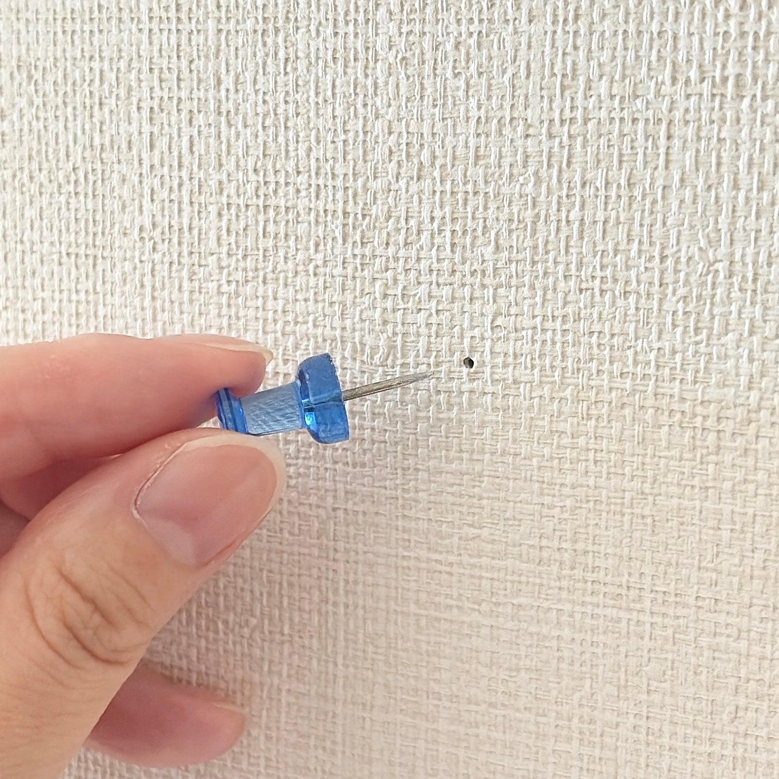 白い壁に指で押しピンを刺す様子。壁には小さな穴が開いています。