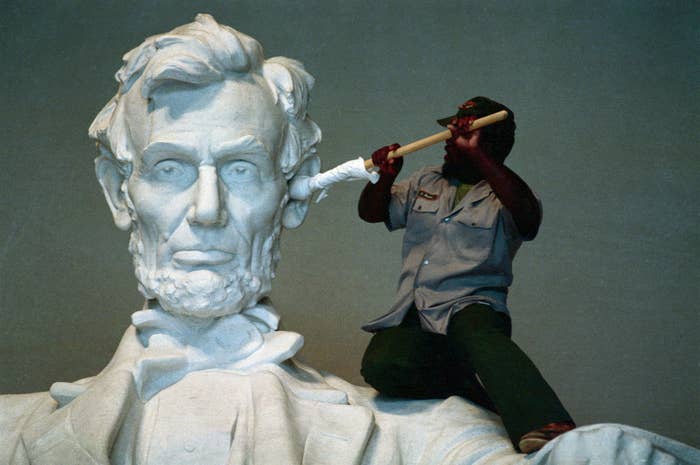 Worker cleans the large ear of the Abraham Lincoln statue at the Lincoln Memorial, using a long brush, illustrating maintenance efforts