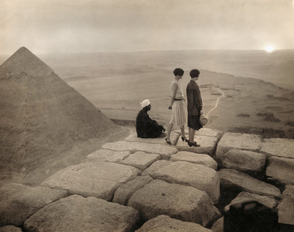 Two women and a guide stand atop the Pyramid of Giza, overlooking a vast landscape at sunset