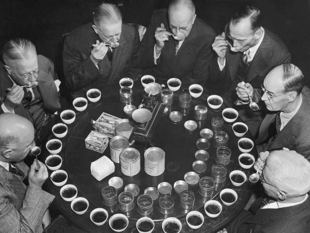 A group of men sit around a table, tasting and evaluating various samples of coffee placed in front of them