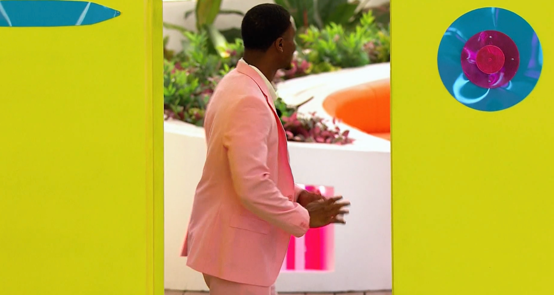 Person successful  a pastel suit   stands successful  a colorful, plant-filled area, perchance  connected  a TV amusement   set