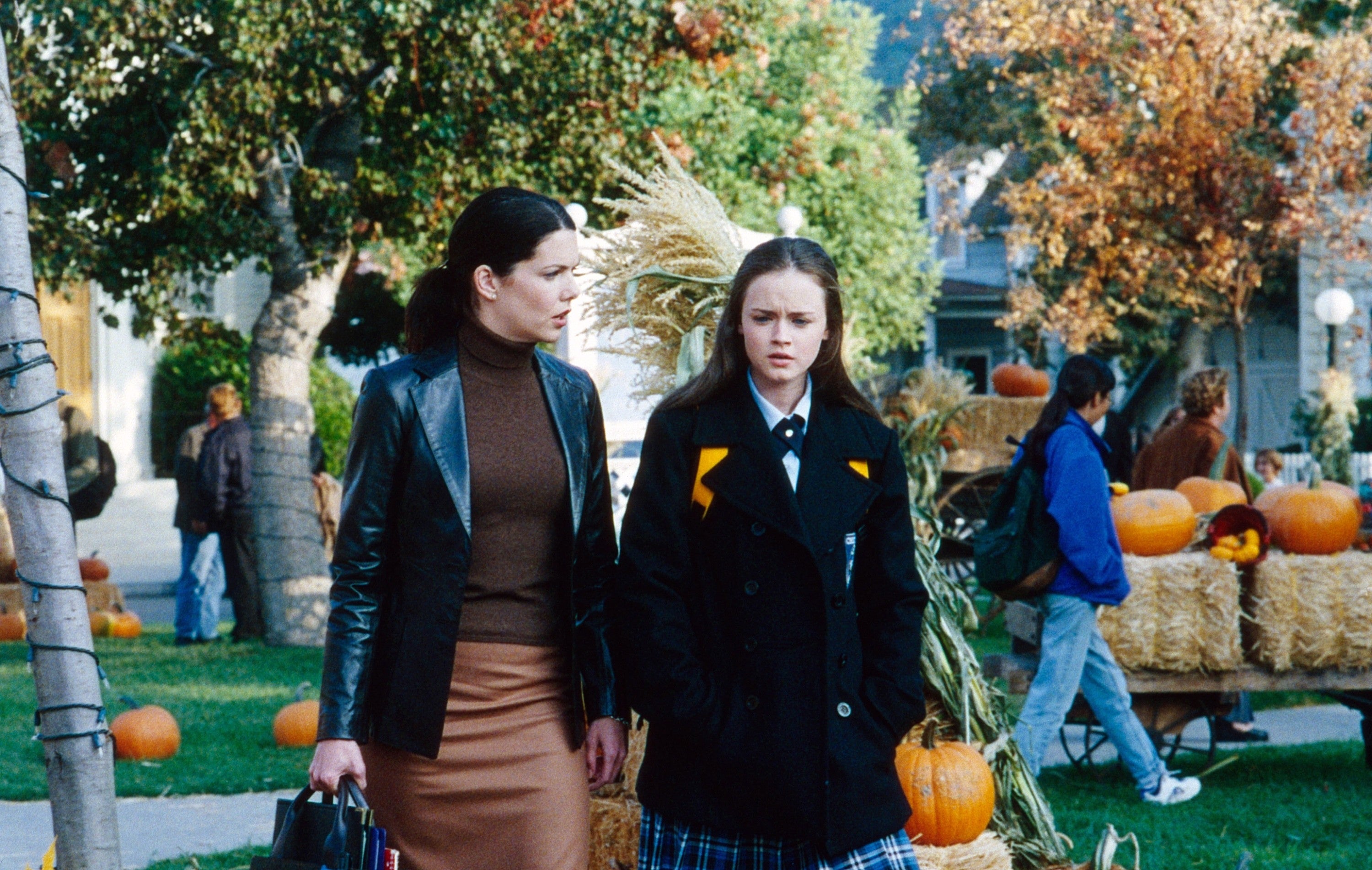 Two women in fall attire walk through a festive pumpkin patch outdoor setting