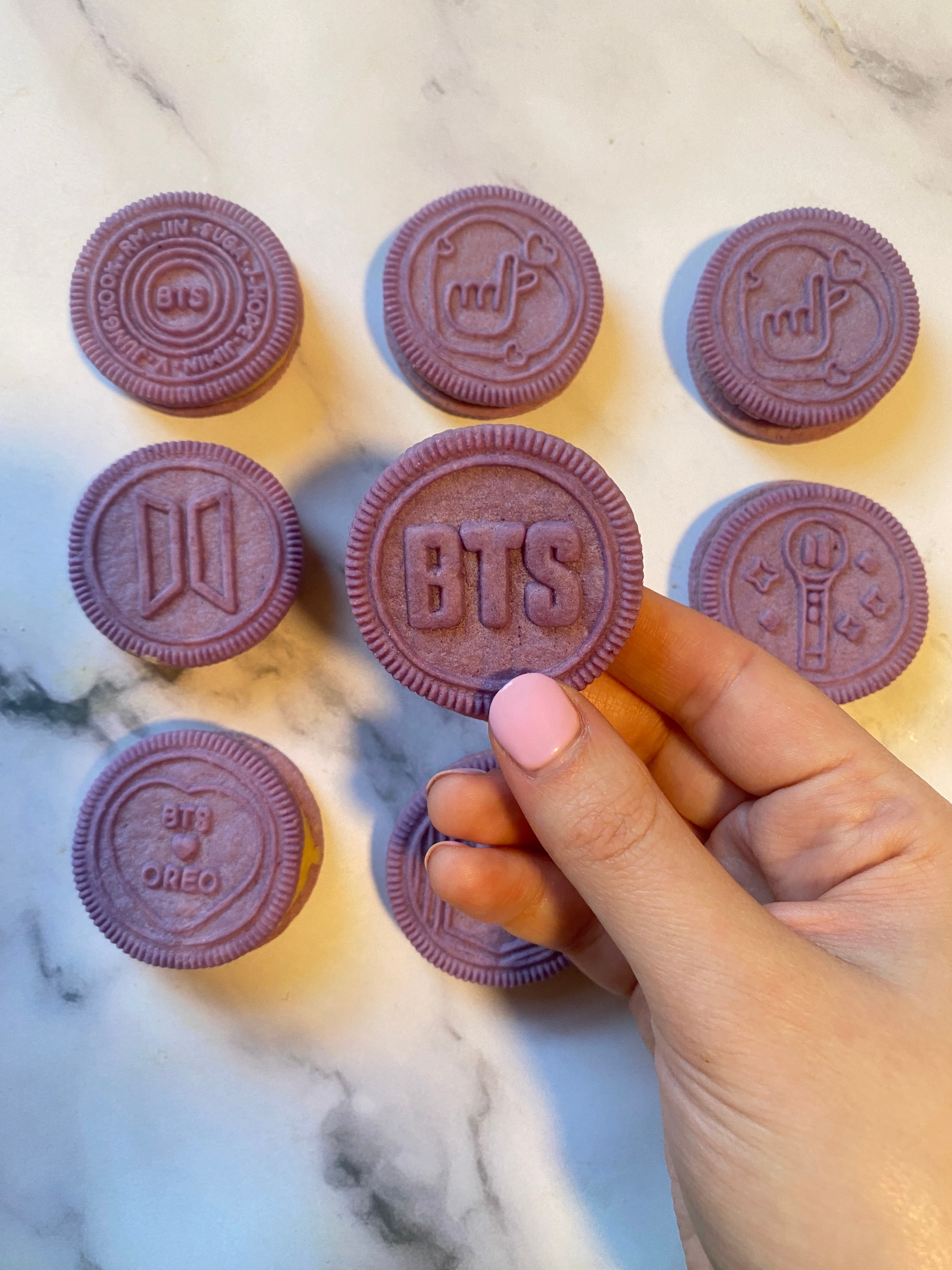 Hand holding a purple Oreo cookie with BTS and other BTS-themed designs in the background