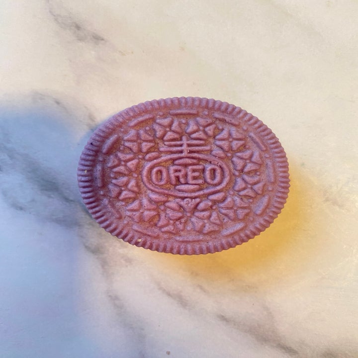 A pink Oreo cookie with detailed floral and company logo design on a marble surface