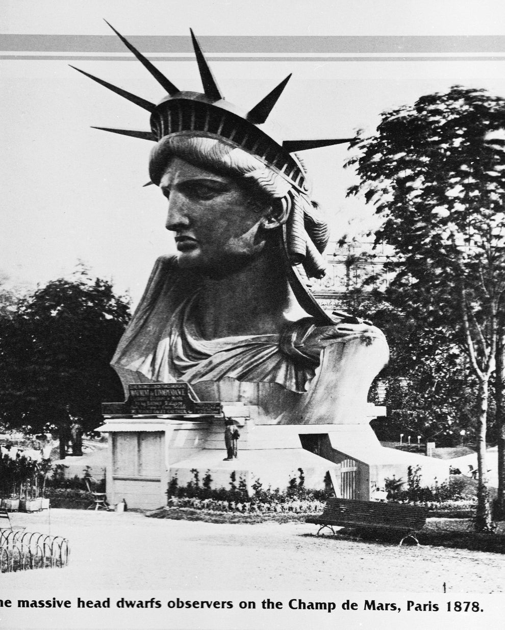 Historic photo of the Statue of Liberty's head on display at Champ de Mars, Paris, 1878, with people standing around for scale