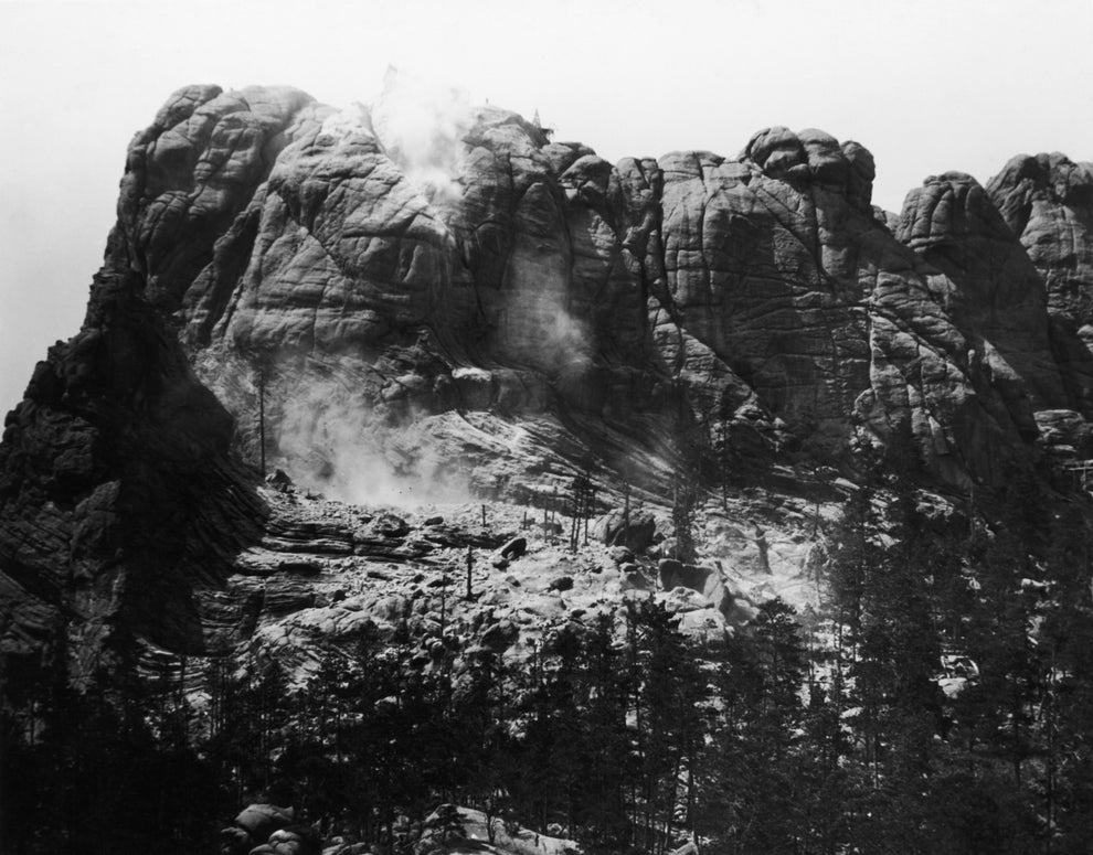 Rocky mountain landscape with scattered trees and dust or smoke rising, possibly from a landslide or excavation