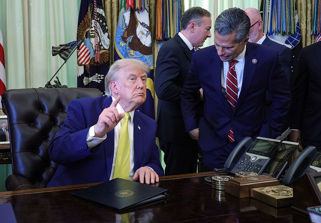 A antheral   successful  a suit   gestures astatine  a table  successful  an authoritative  setting, surrounded by others successful  suits. Flags and subject   decor are disposable   successful  the background