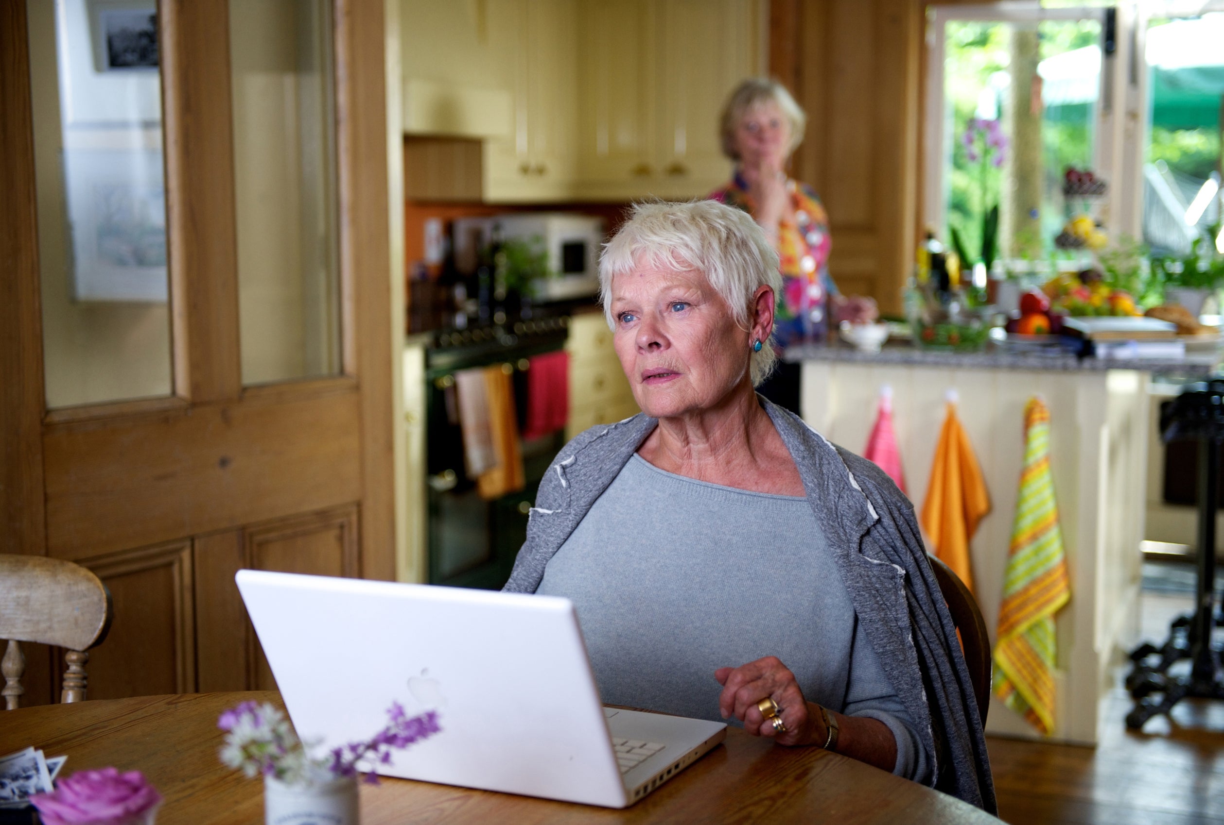 An older pistillate seated astatine a table, focusing connected a laptop, with different idiosyncratic successful the room background