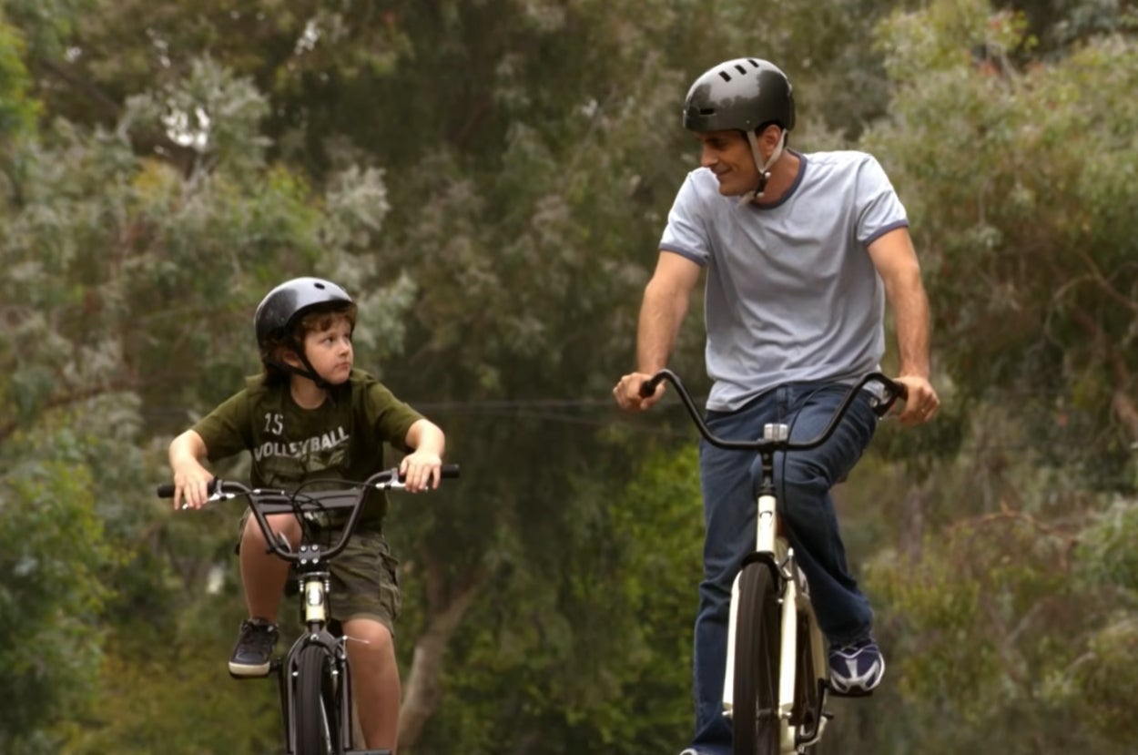 Phil and Luke Dunphy from "Modern Family" wearing helmets riding bicycles outdoors