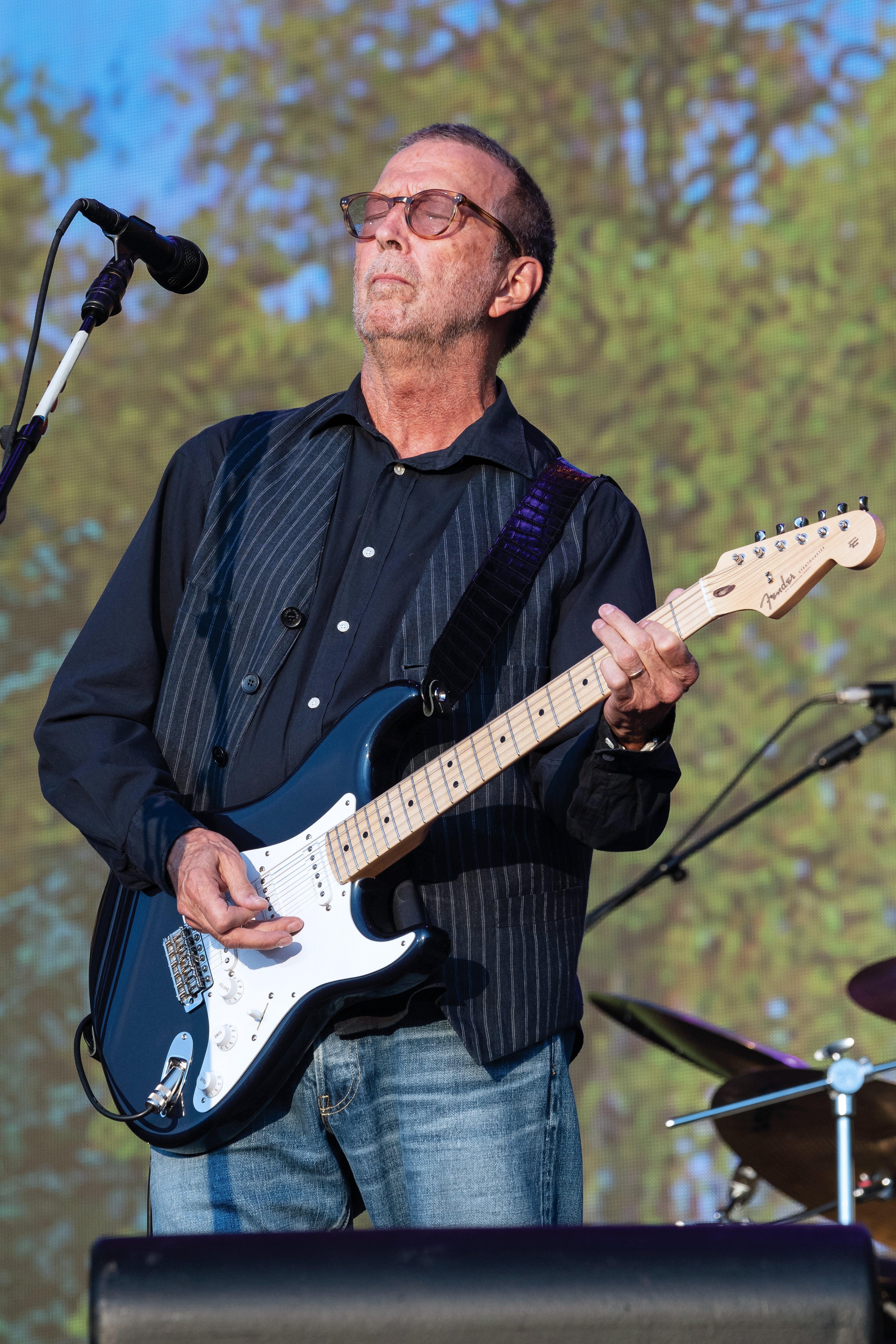 Musician wearing a striped vest over a shirt plays an electric guitar on stage outdoors