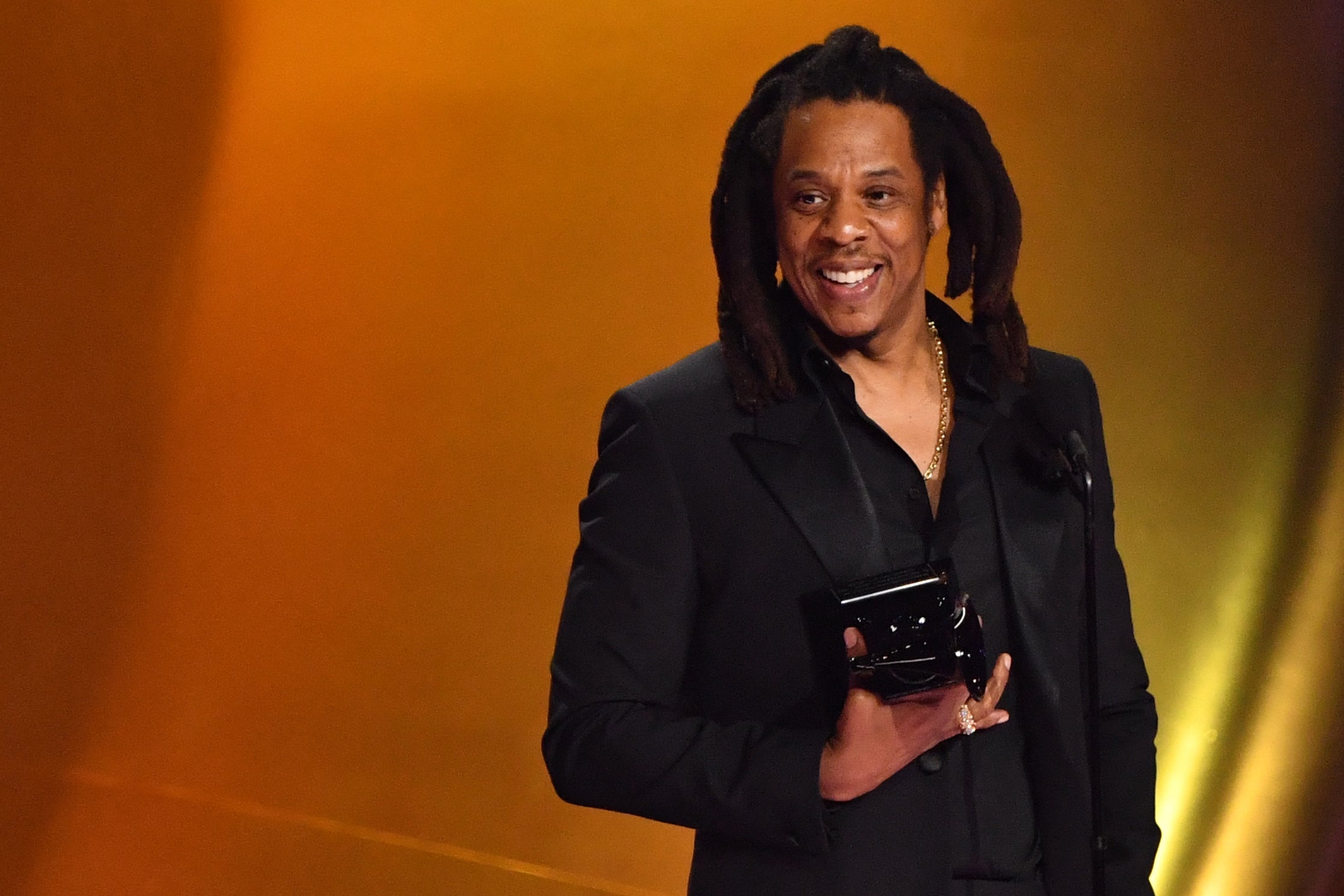 Person in a black suit on stage holding an award, smiling during an event