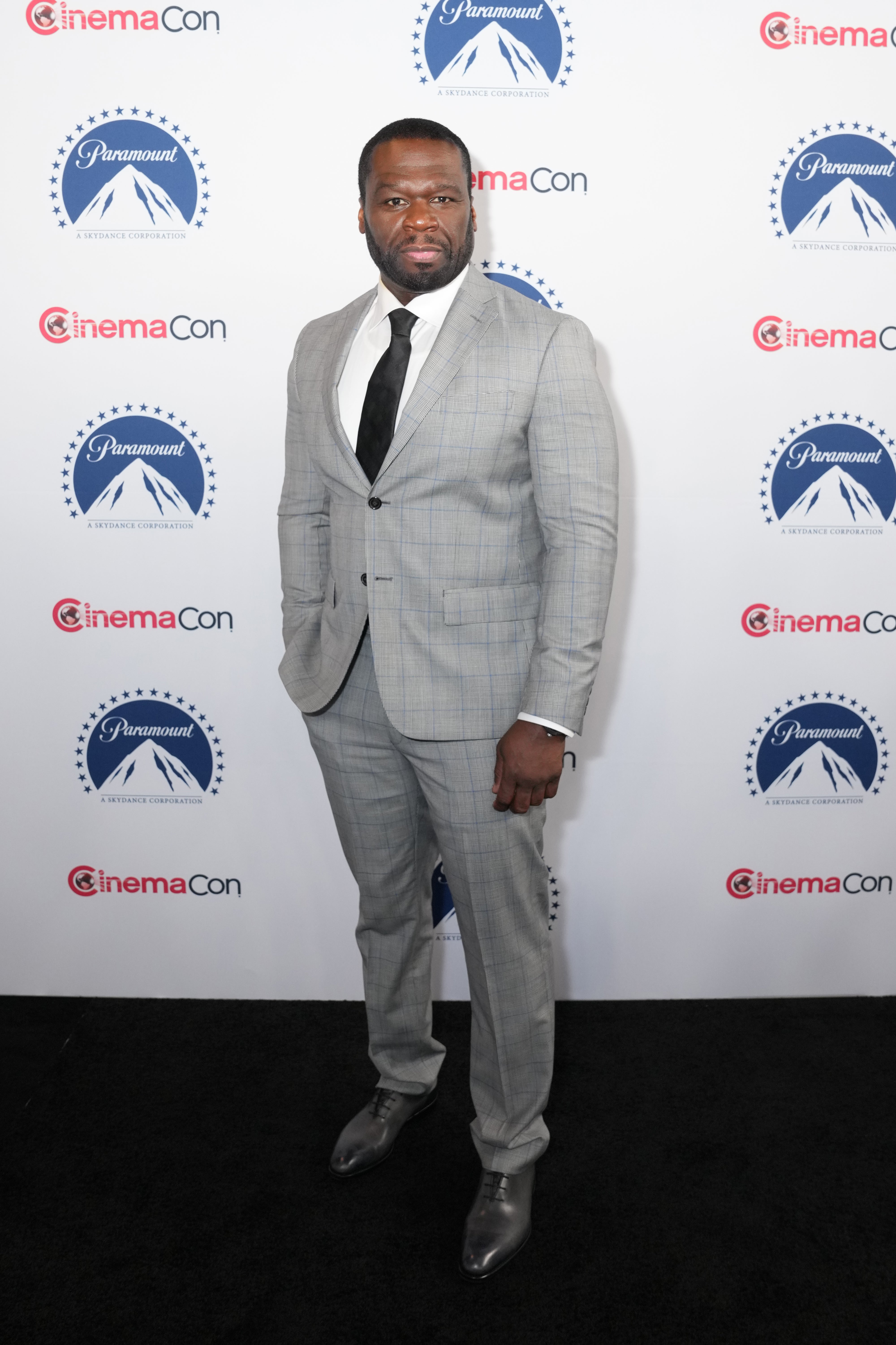 A person in a gray suit with a white shirt and black tie at a media event backdrop featuring Paramount and CinemaCon logos
