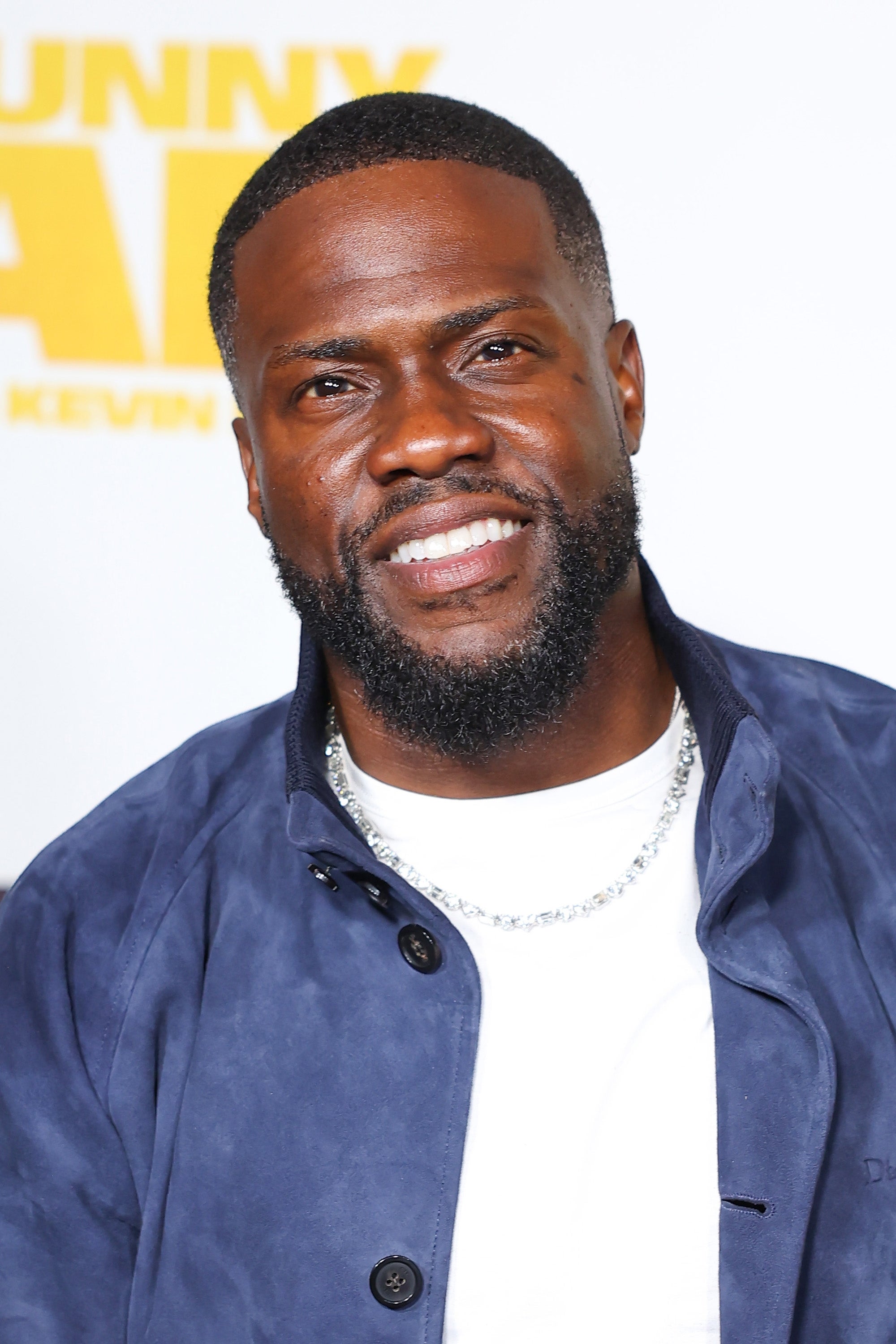 A man in a casual jacket smiles at a promotional event backdrop