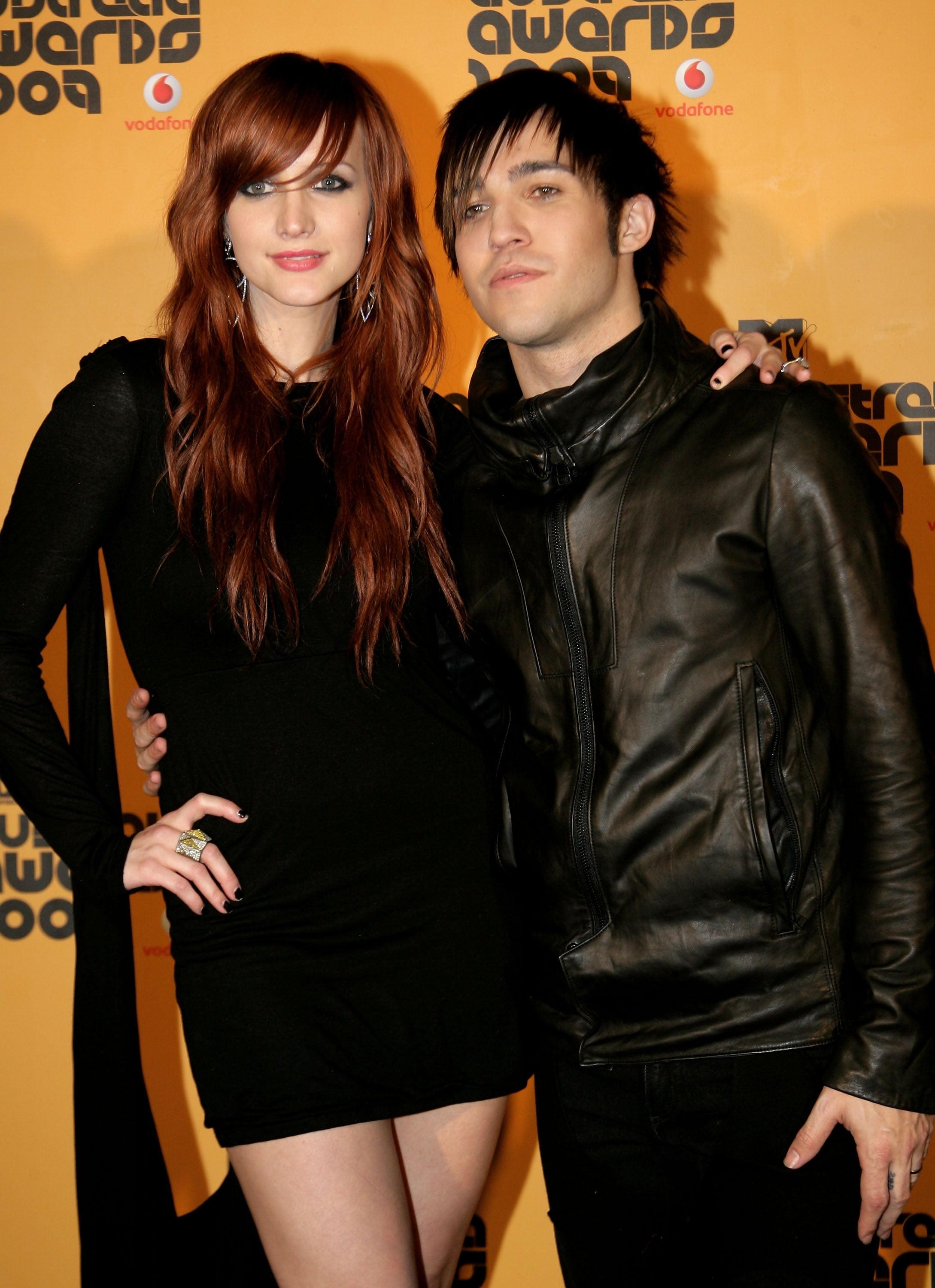 Two people on a red carpet; one in a black dress, the other in a leather jacket