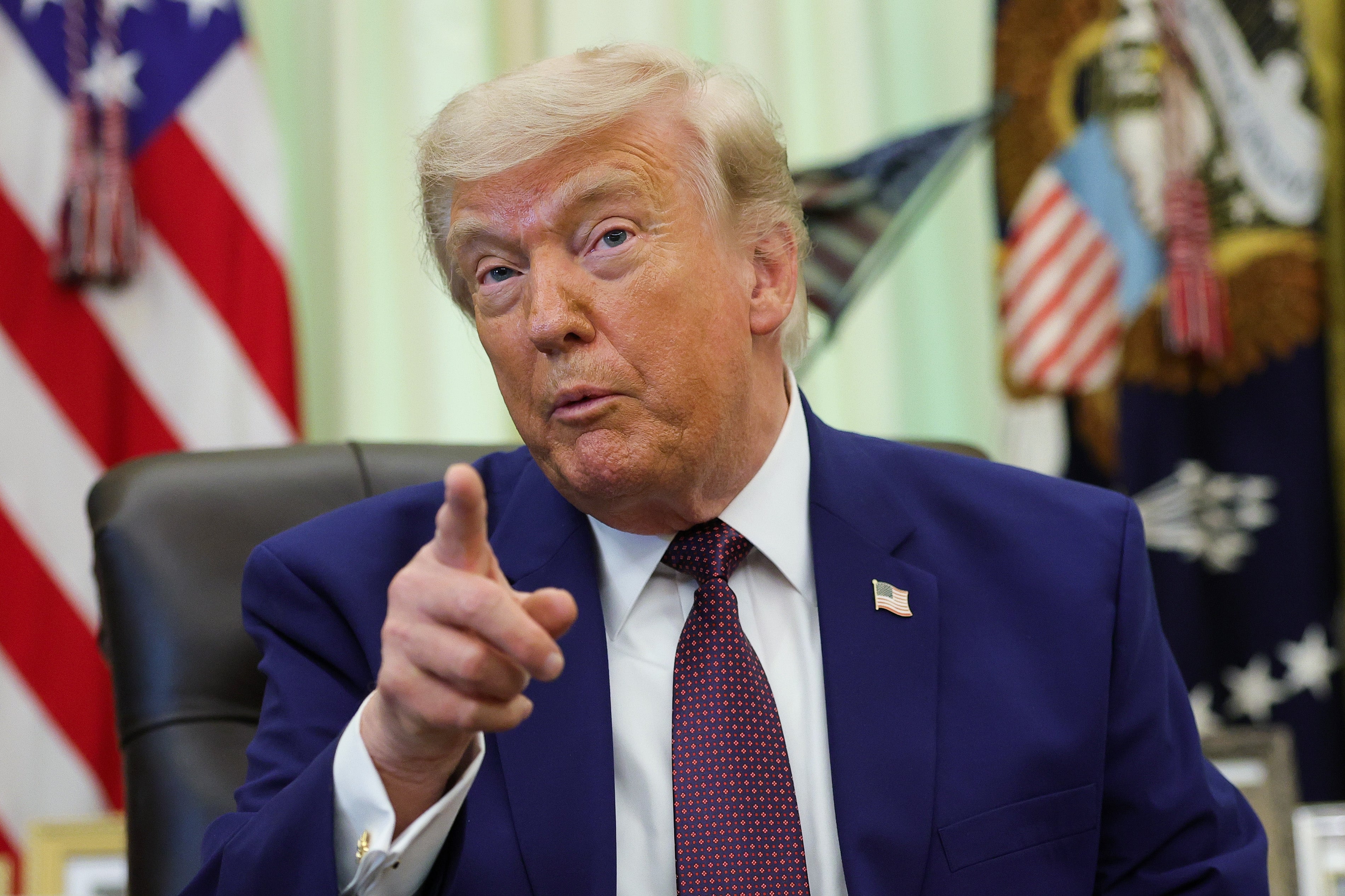 A idiosyncratic   successful  a suit   gestures portion    seated successful  an bureau   mounting  with flags successful  the background