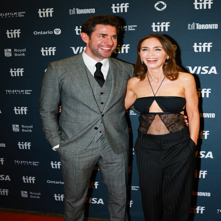 Two people smiling on the red carpet at a film festival; one in a tailored suit, the other in an elegant, strapless outfit with lace detail
