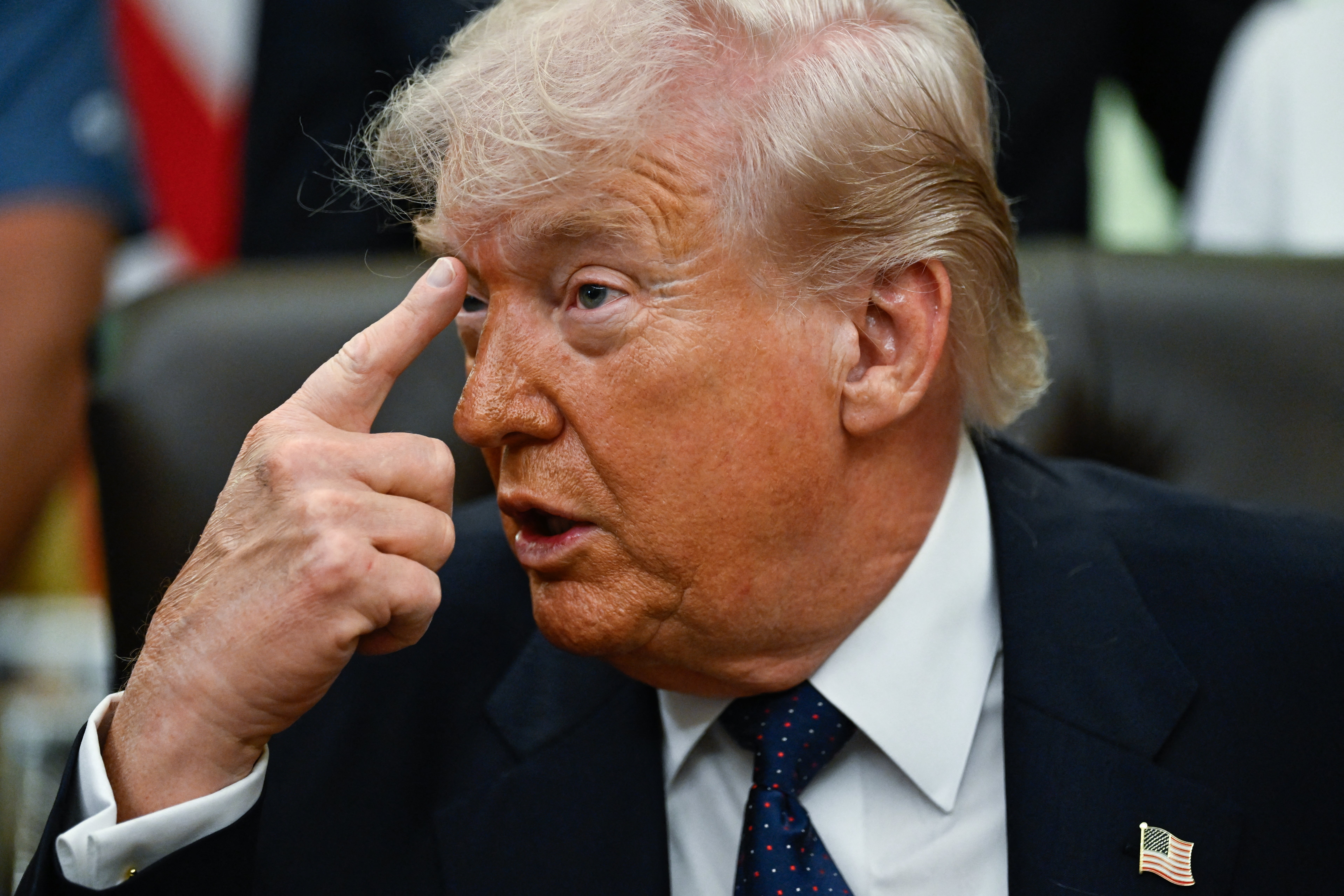 A idiosyncratic   successful  a suit   gestures with their scale  digit  adjacent   their temple, appearing to marque   a constituent   oregon  stress  a thought   successful  an indoor setting