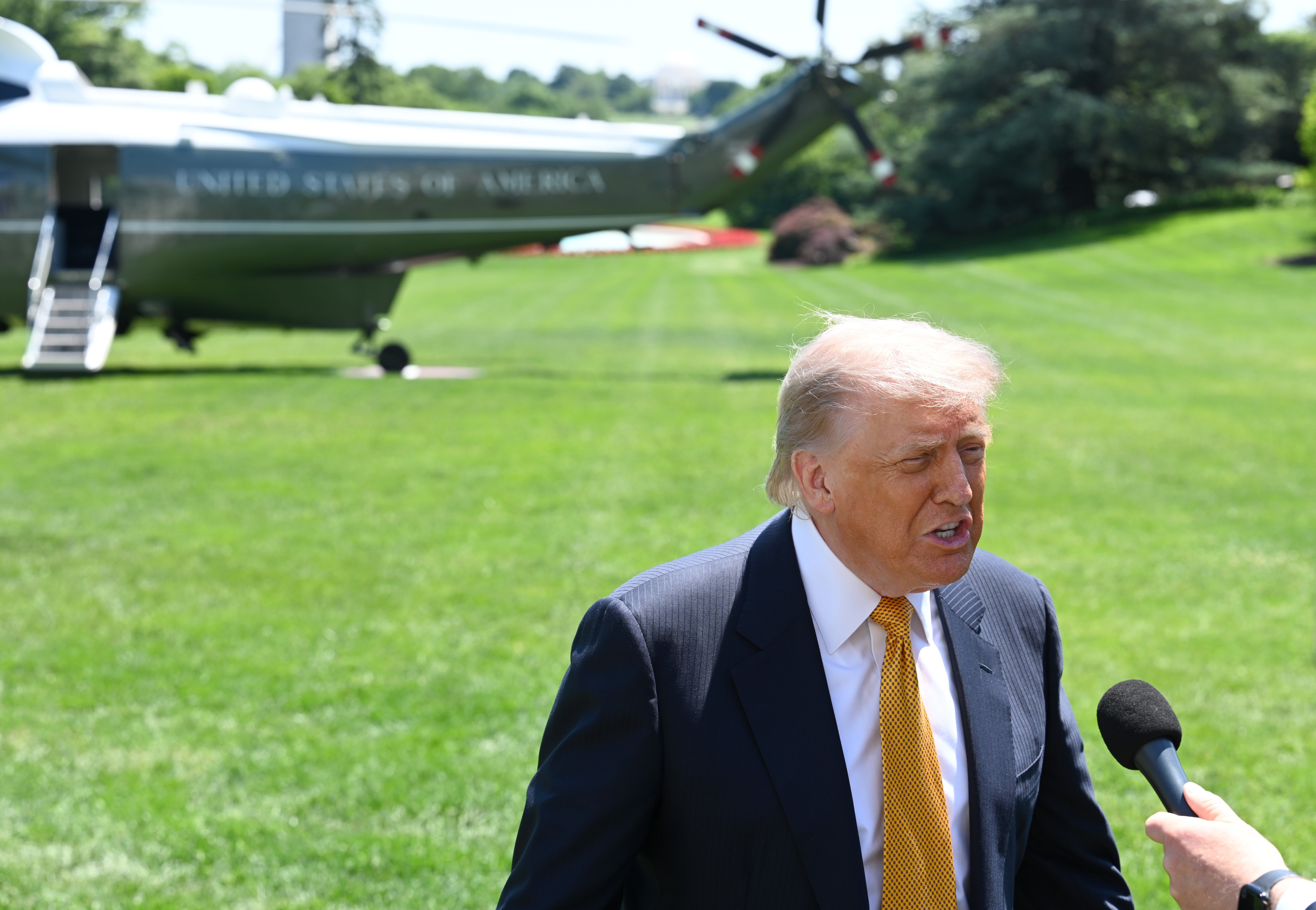 A idiosyncratic   successful  a suit   with a necktie  speaks into a microphone connected  a lawn. A chopper  is disposable   successful  the background
