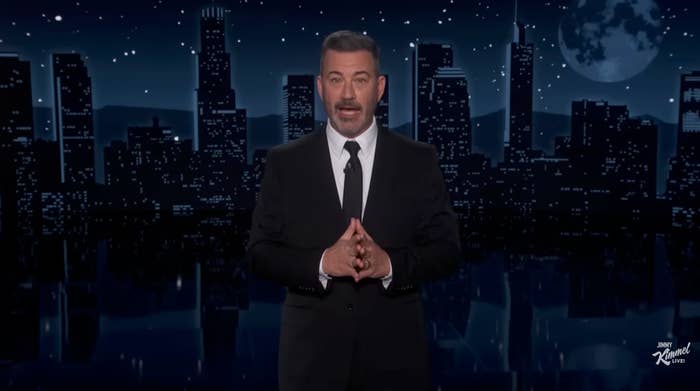A antheral   successful  a suit   stands connected  a signifier    with a metropolis  skyline backdrop, speaking oregon  hosting a TV show