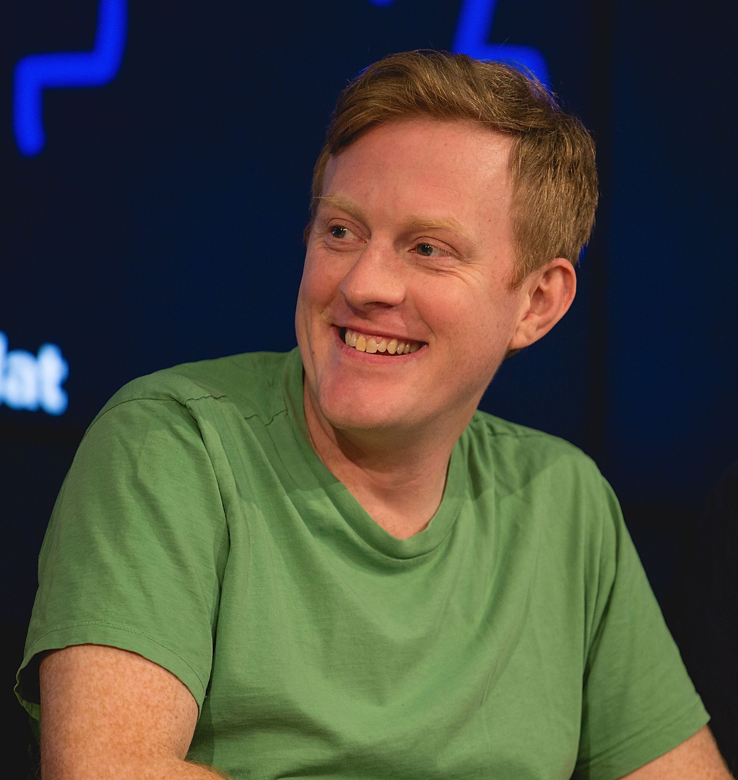 Person smiling, wearing a casual green shirt, seated on stage at an event